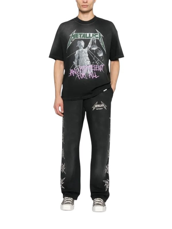 Wearing a black Metallica t-shirt and Represent MLM4376 40 Year Anniversary Pants Blk with an elasticated waistband, they stand against a white background, each printed design enhancing their unique style.