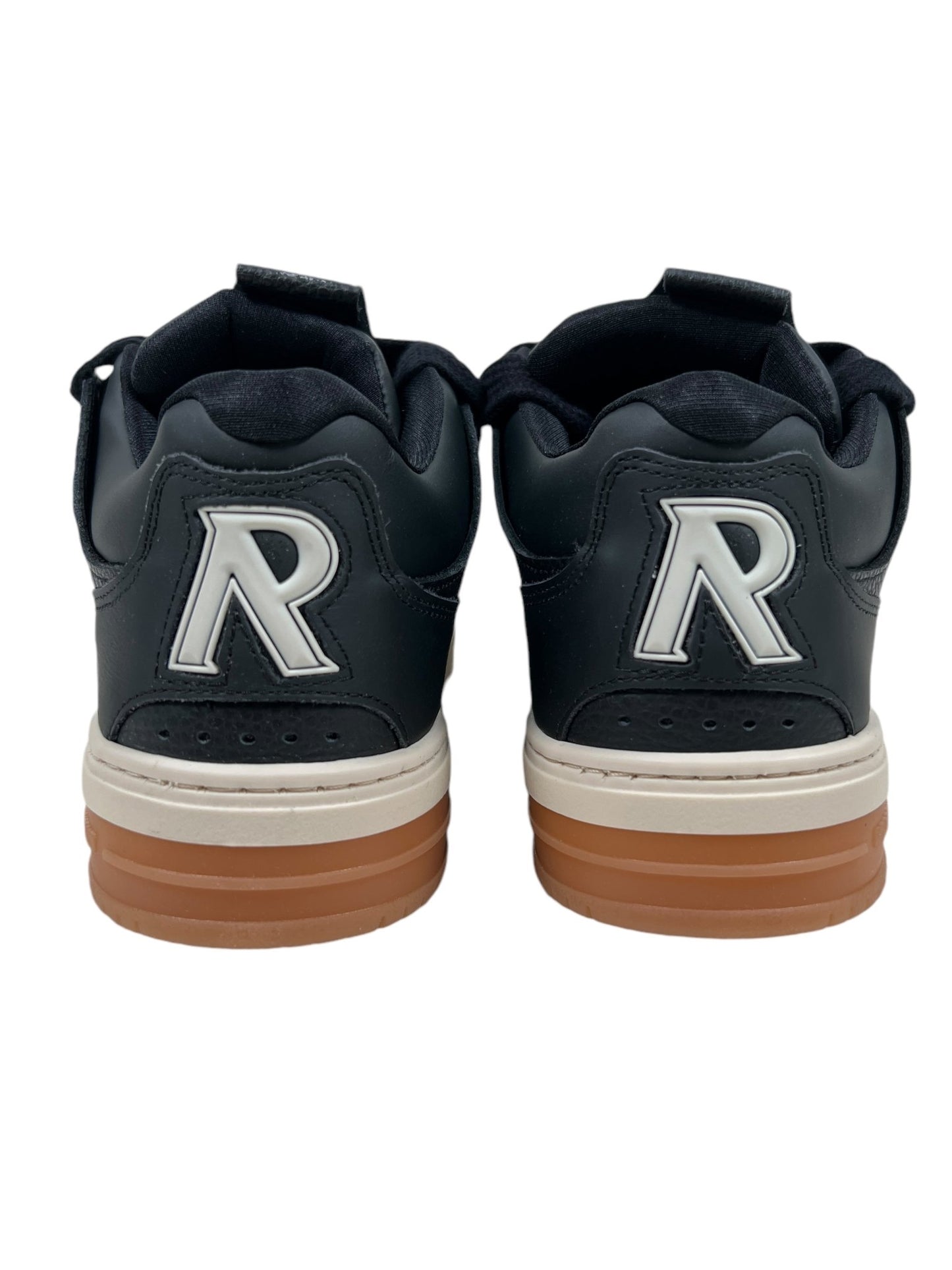 The rear view showcases the Represent MLM9599 BULLY BLACK/GUM sneakers, highlighting their distinctive features such as a striking silver "R" logo on the back and gum-colored soles. The sleek design is further elevated by contrasting TPU overlays.