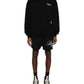 Dressed in a Represent OCM41200 Club Script Hoodie in Black by REPRESENT, along with black shorts and sleek black sneakers featuring white soles, the individual embodies a streetwear vibe against a pristine white backdrop.