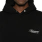 A person is wearing a Represent OCM41200 Club Script Hoodie in Black by REPRESENT, showcasing the "Represent Owners' Club" text on the front, epitomizing streetwear style with its unique buttoned collar.
