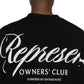 Back view of a person wearing the Represent OCM41201 Club Script T-shirt in black, showcasing "Represent Owners' Club" in crisp white letters, highlighting their unique style.