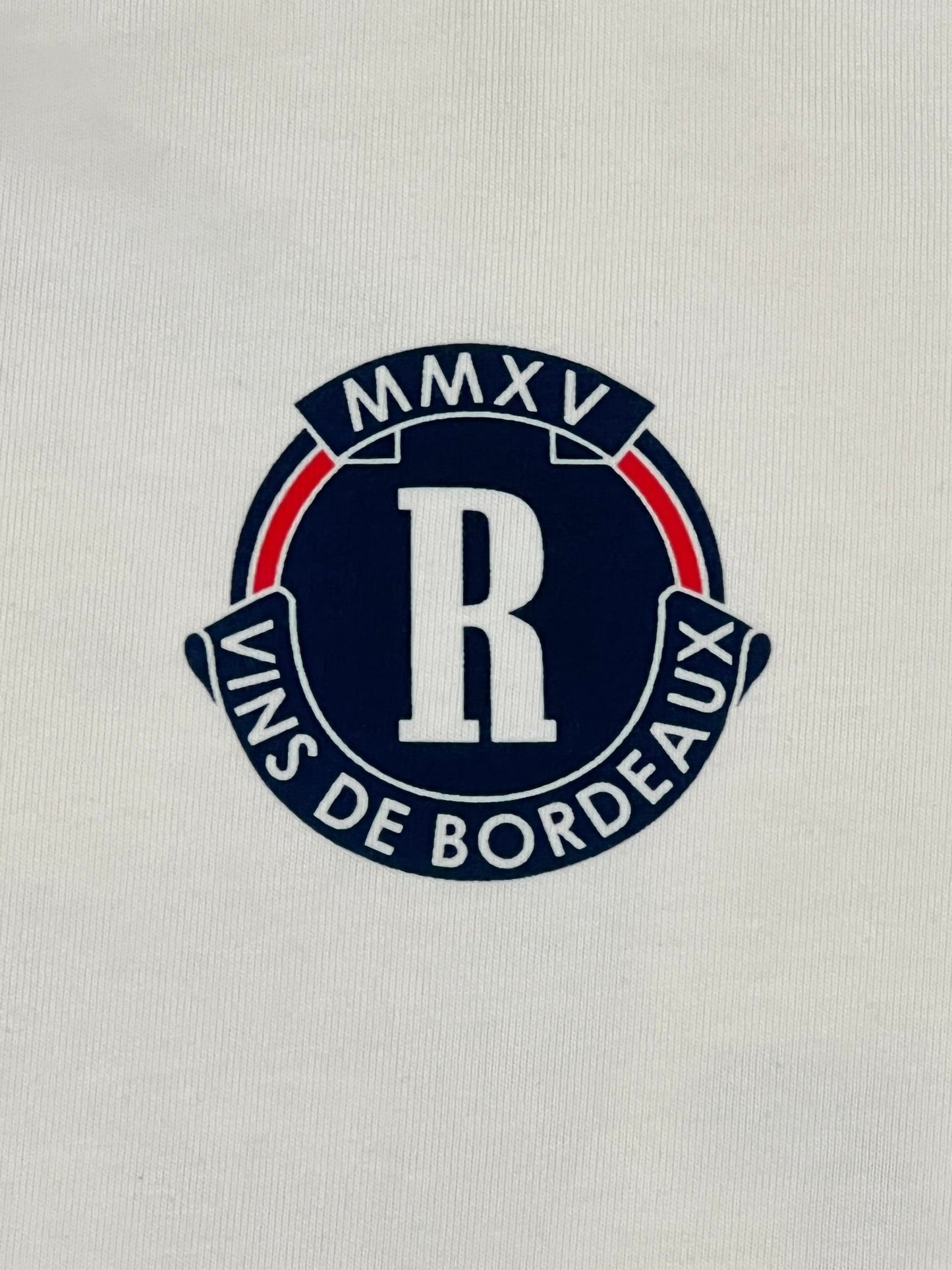 The Rhude Bordeaux Wine Tee in vintage white showcases a logo with the letter "R" encircled, accompanied by the words "Vins de Bordeaux" and "MMXV." This graphic design is perfect for a RHUDE t-shirt crafted from 100% cotton.