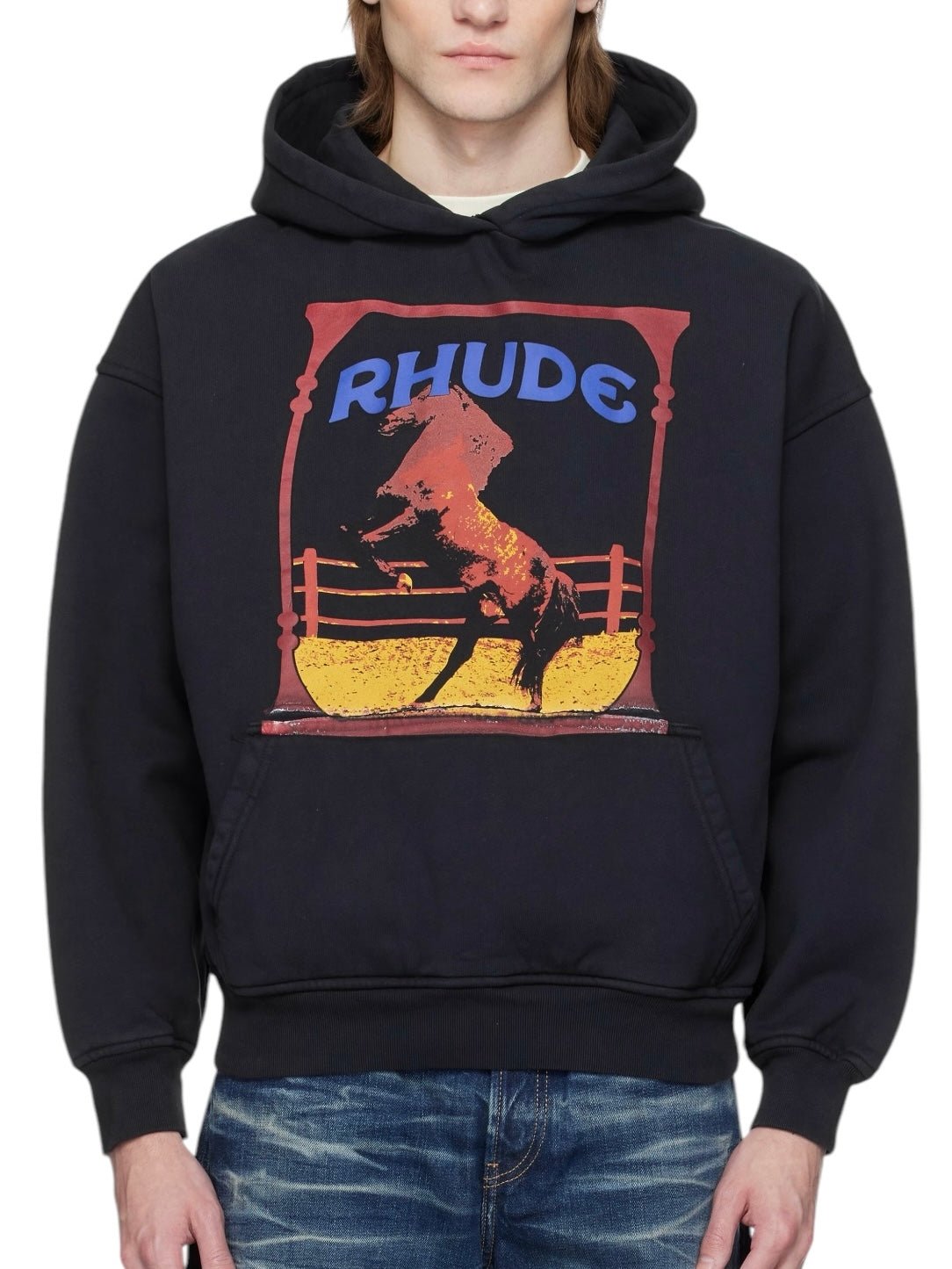 A person wearing the Rhude Cadre Hoodie Black, a black RHUDE cotton fleece hoodie with a bold horse logo and "RHUDE" graphic, paired it effortlessly with blue jeans. The hoodie’s practical kangaroo pocket added both style and functionality to the look.