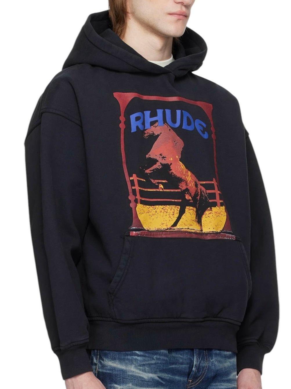 A person wearing the Rhude Cadre Hoodie Black with a colorful horse and "RHUDE" logo on the front. This cozy cotton fleece design includes a kangaroo pocket, blending style and function.