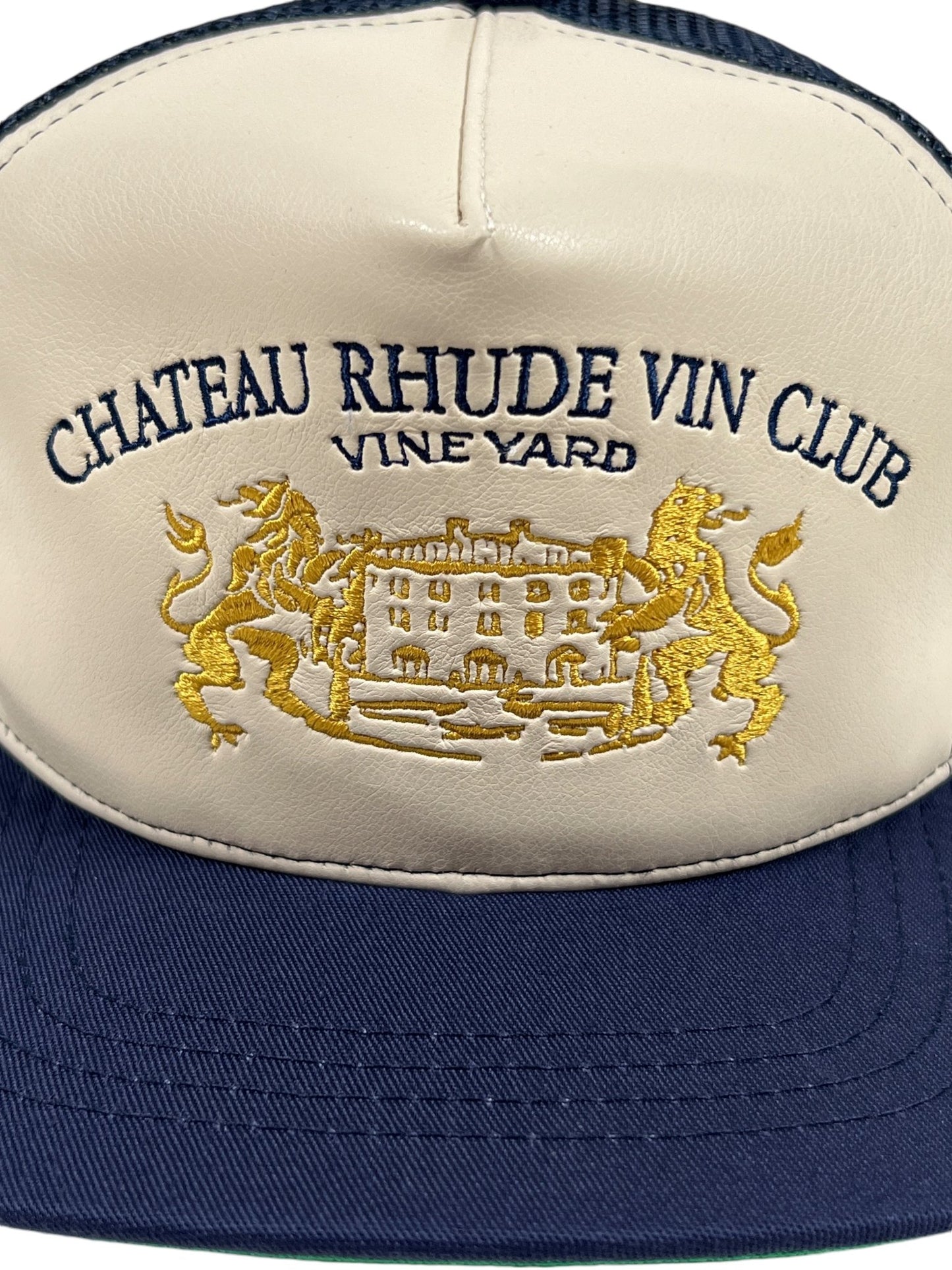 RHUDE CELLIER trucker hat in navy and cream, featuring "Chateau Rhude Vin Club Vineyard" and a castle design embroidered in gold, with an embroidered leather detail.