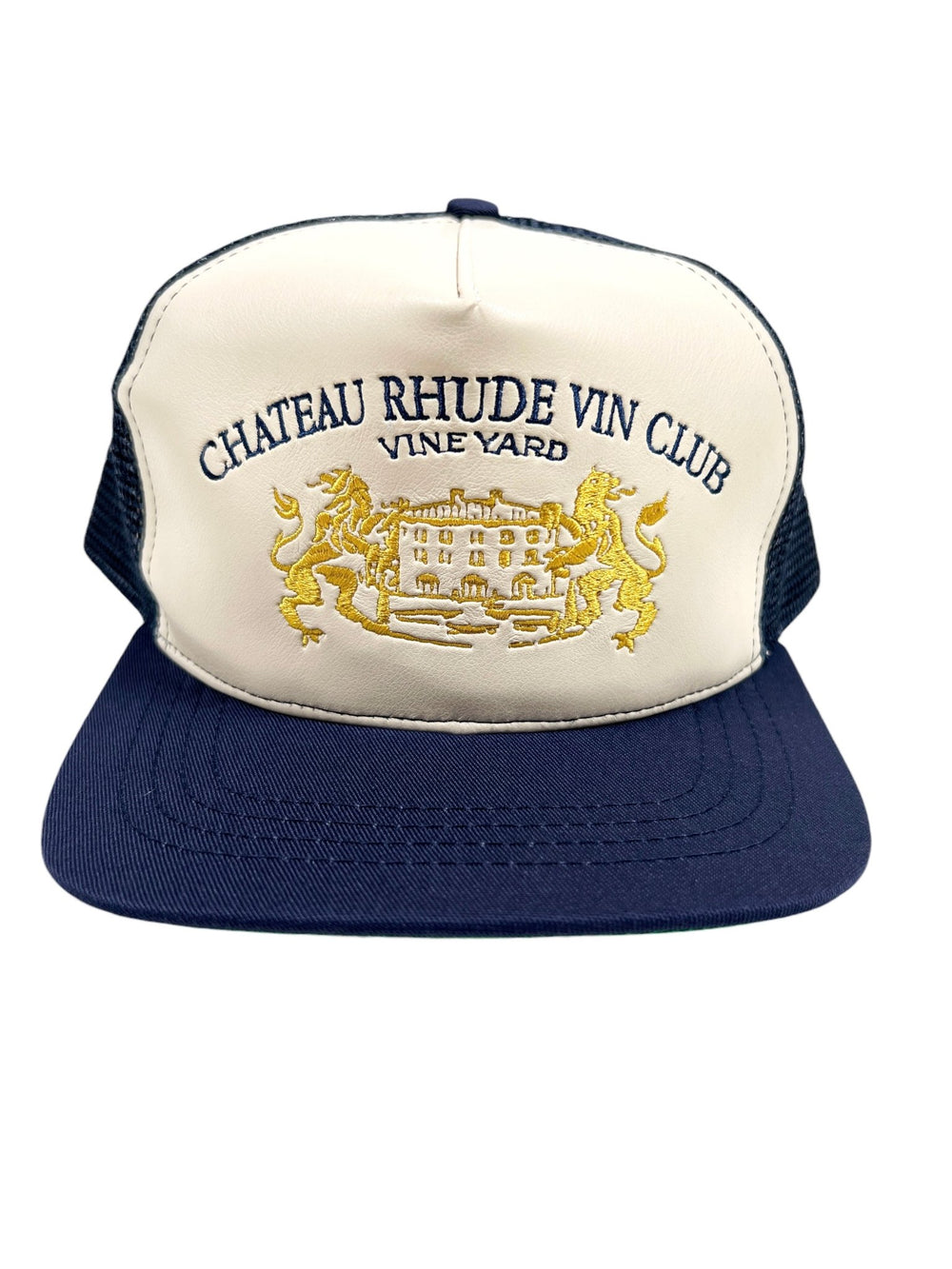 The RHUDE CELLIER TRUCKER HAT NAVY/CREAM features embroidered text reading "Chateau Rhude Vin Club Vineyard" above an image of a chateau flanked by two lions, and includes an embroidered leather detail for added style.