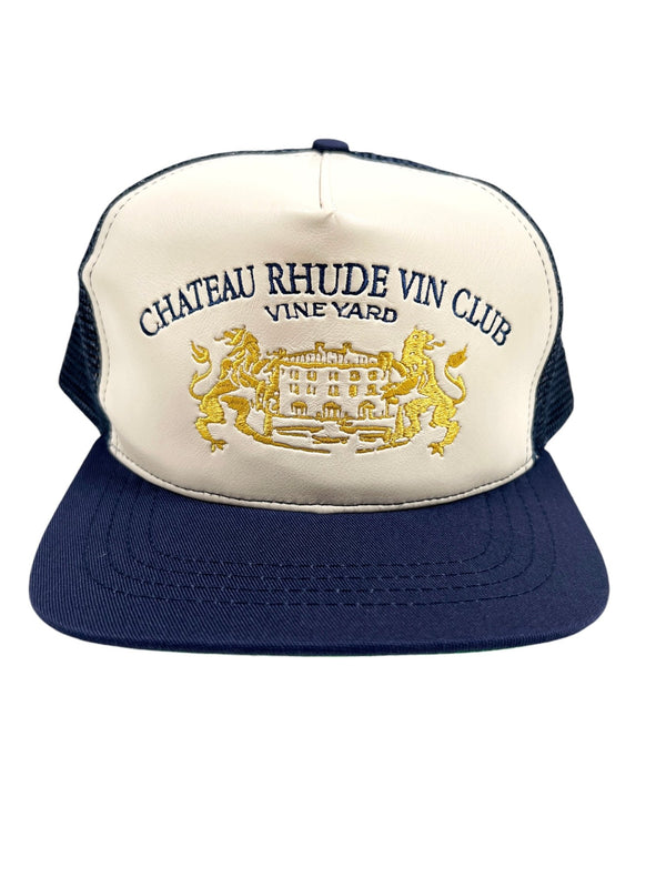 The RHUDE CELLIER TRUCKER HAT NAVY/CREAM features embroidered text reading "Chateau Rhude Vin Club Vineyard" above an image of a chateau flanked by two lions, and includes an embroidered leather detail for added style.