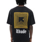 A person is wearing the Rhude Chevron Logo Repeat Tee in vintage black, featuring a geometric yellow design and "Rhude" text on the back, along with the striking Rhude Chevron Box logo.