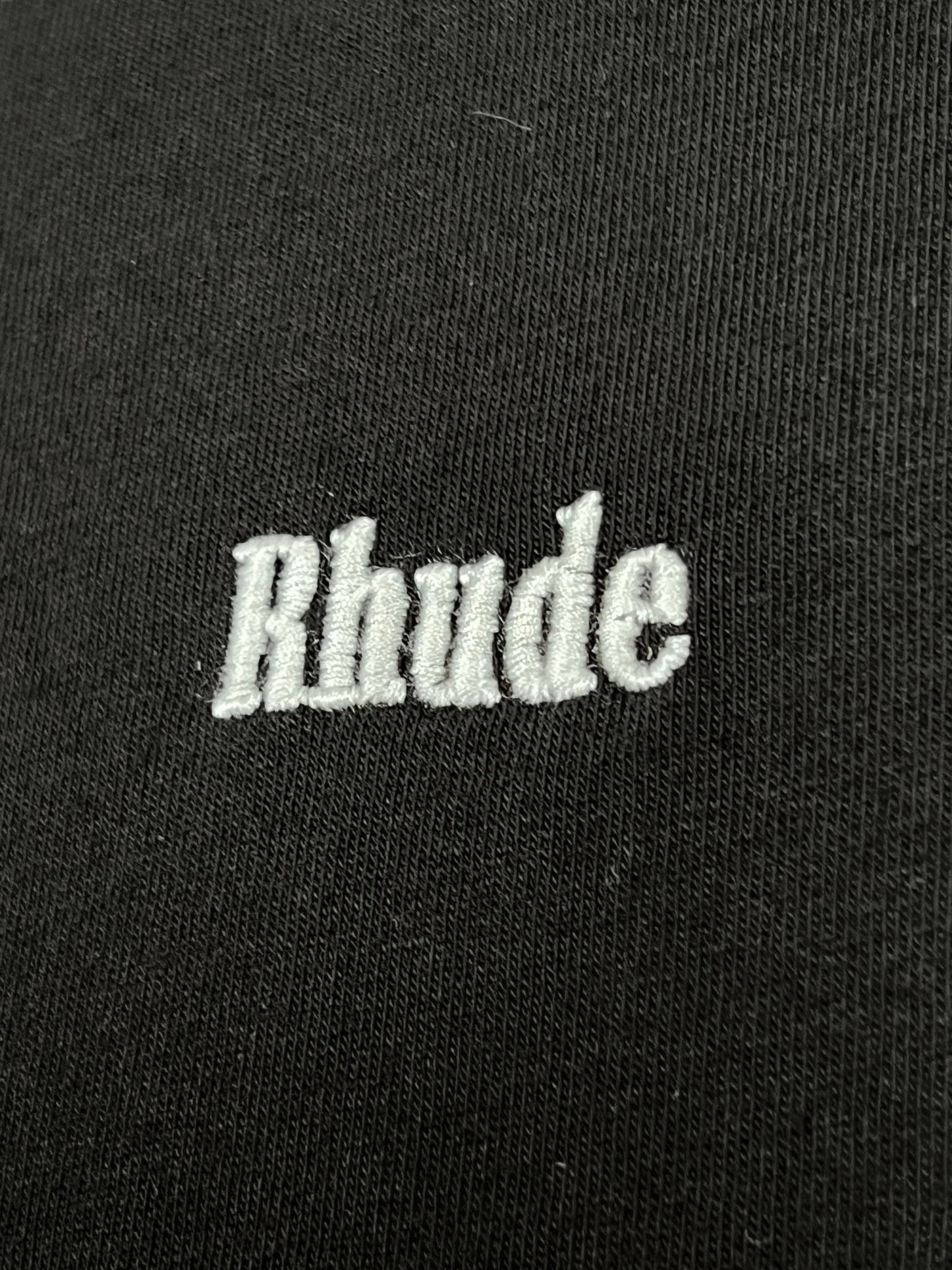 Close-up of the Rhude Classique Reverse Ls Tee in black, designed by RHUDE, showcasing white embroidered text "Rhude.