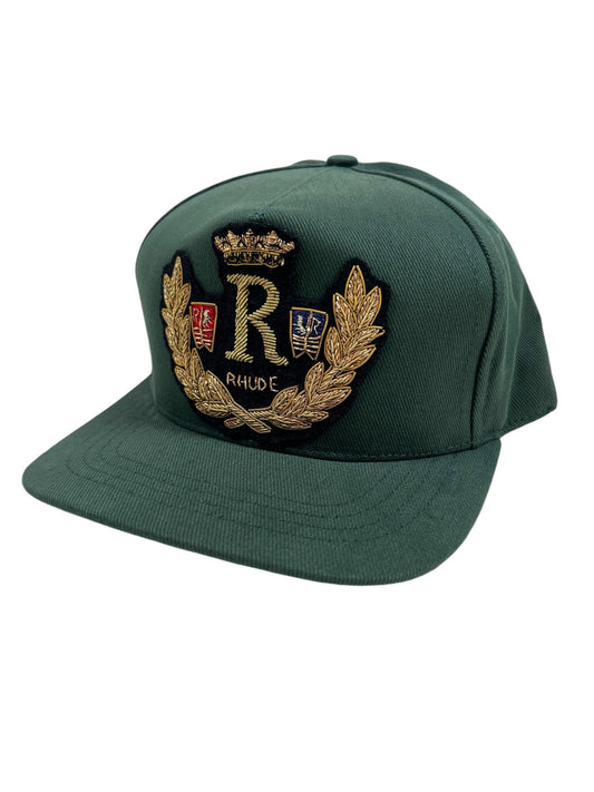 The RHUDE DIANA CREST HAT in green boasts an embroidered design with a crowned "R," two shields, and laurel wreaths.