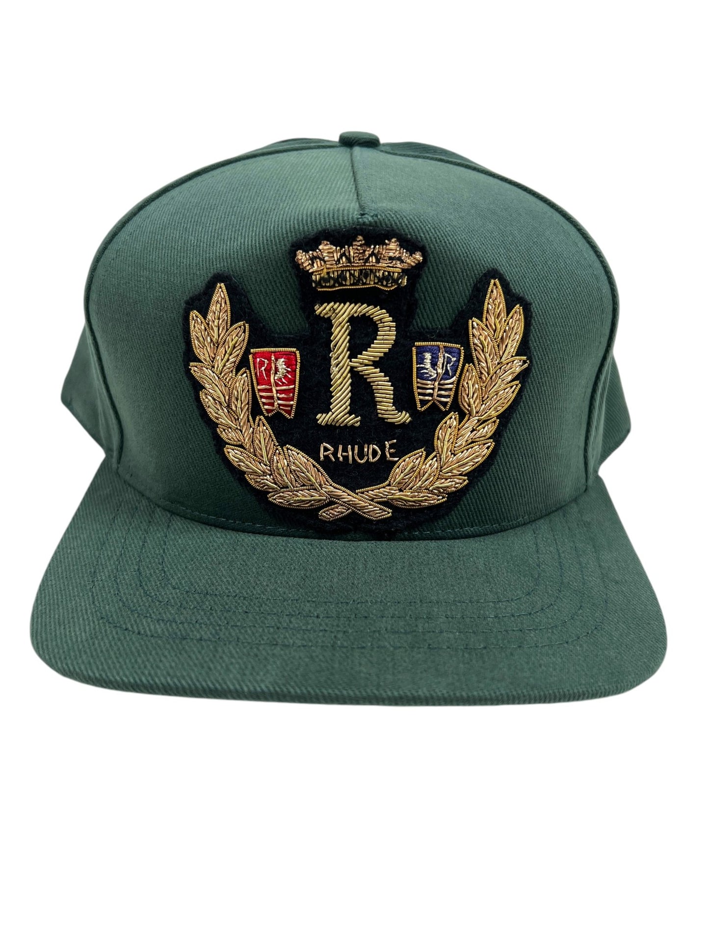 The RHUDE DIANA CREST HAT GREEN by RHUDE is a stylish green baseball cap featuring a gold embroidered "R" surrounded by a laurel wreath, shields, and a crown, along with the text "RHUDE." This accessory is reminiscent of the Diana crest hat.