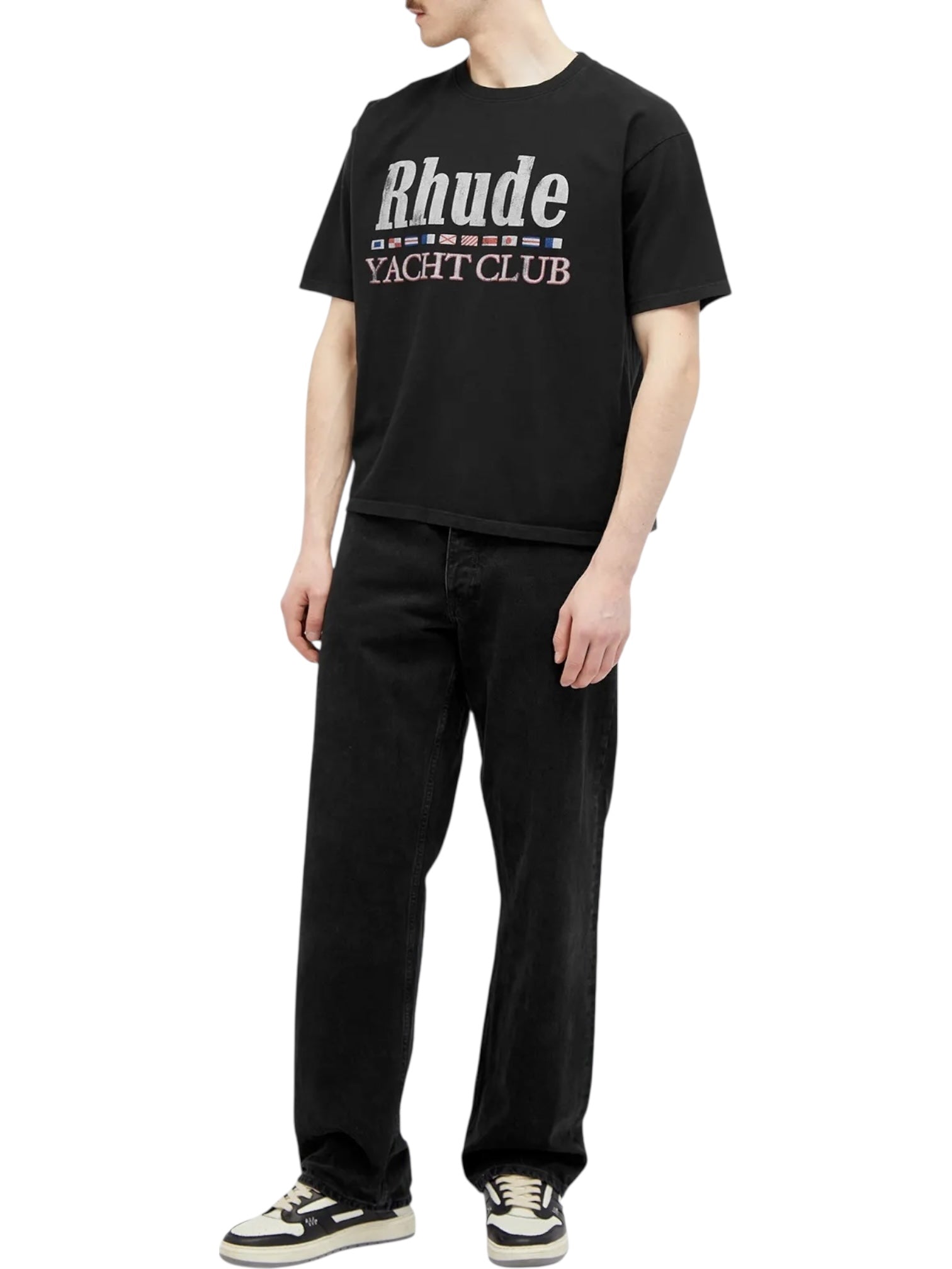 A person in the RHUDE FLAG TEE BLK by RHUDE, paired with black pants and black-and-white sneakers, stands against a white background, highlighting the tee’s bold American-themed graphics.