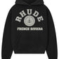 The Rhude French Riviera Hood Black from RHUDE showcases gray "RHUDE FRENCH RIVIERA" text, a racing emblem graphic with "WORLD CHAMPIONSHIP TEAM RACING" text, and has a kangaroo pocket.