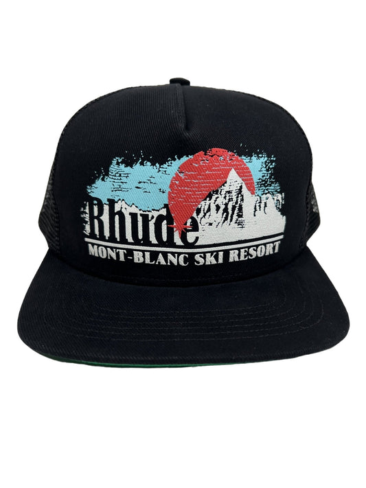 RHUDE MONT-BLANC TRUCKER HAT BLACK with a printed design featuring a red sun, blue sky, mountains, and the text “Rhude Mont-Blanc Ski Resort.” This stylish RHUDE hat comes with an adjustable snapback for a perfect fit.