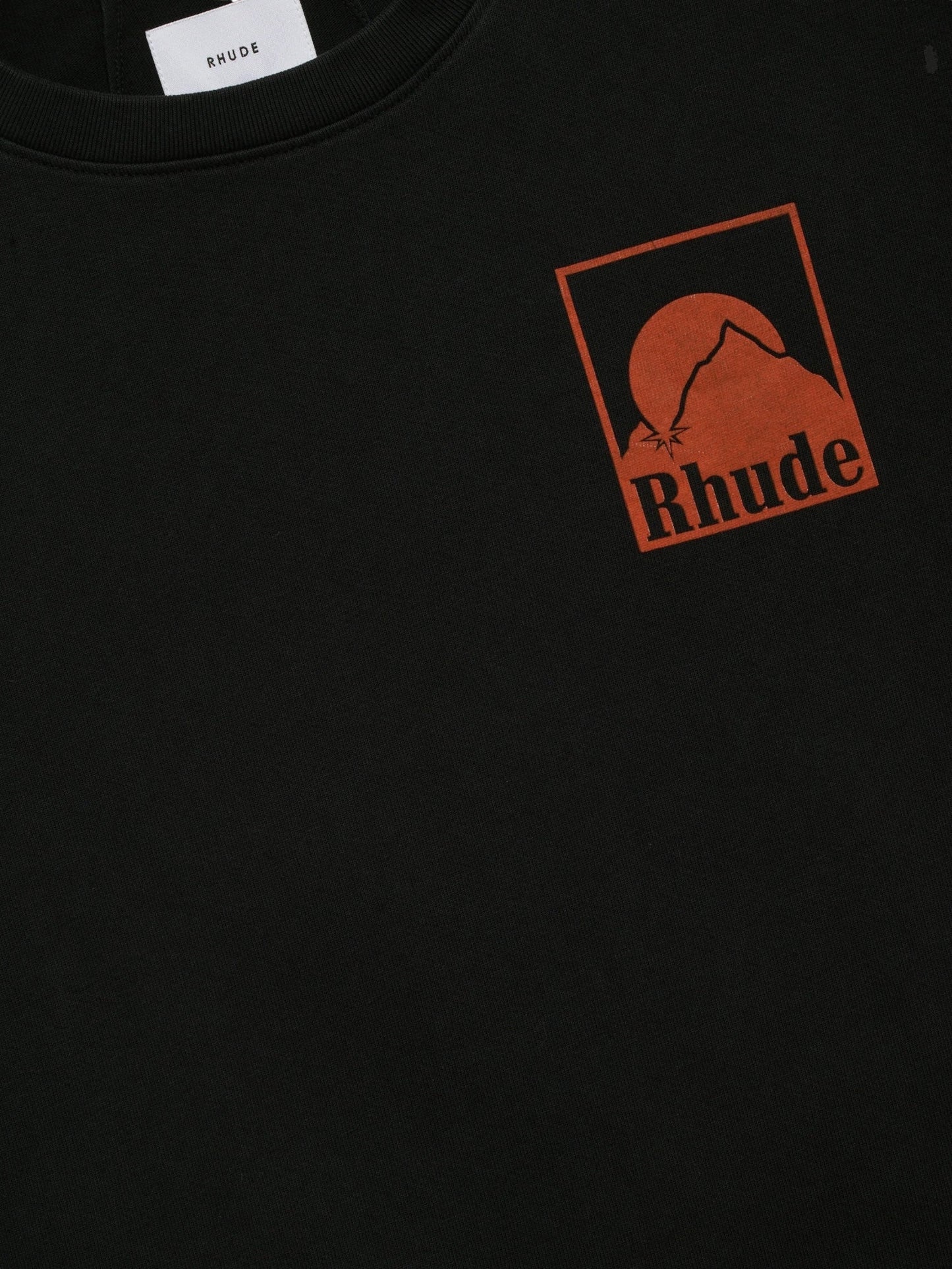 The Rhude Moonlight Badge LS Tee Vtg Black by RHUDE is a boxy-fit, premium washed cotton sweatshirt with an orange mountain and sun graphic and "Rhude" on the chest, inspired by the iconic Moonlight shirt.