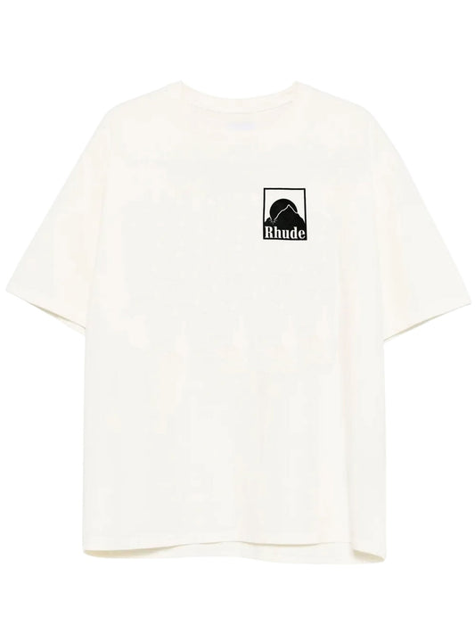 The Rhude Moonlight Badge Tee in white by RHUDE features short sleeves with a sophisticated "Rhude" logo on the left chest, enhanced by a unique Moonlight Badge print.