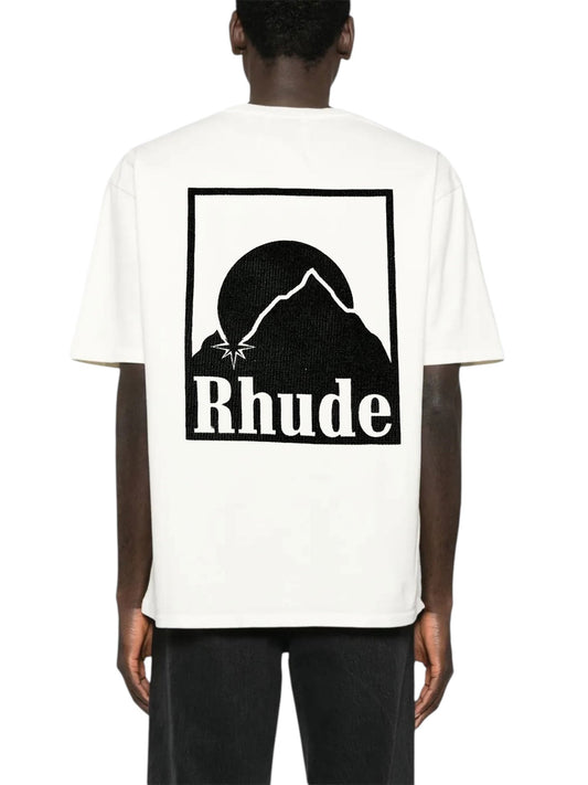 A person in a RHUDE Moonlight Badge Tee features a striking black graphic of a mountain and sun, seamlessly incorporating the iconic "Moonlight Badge" print on the back.