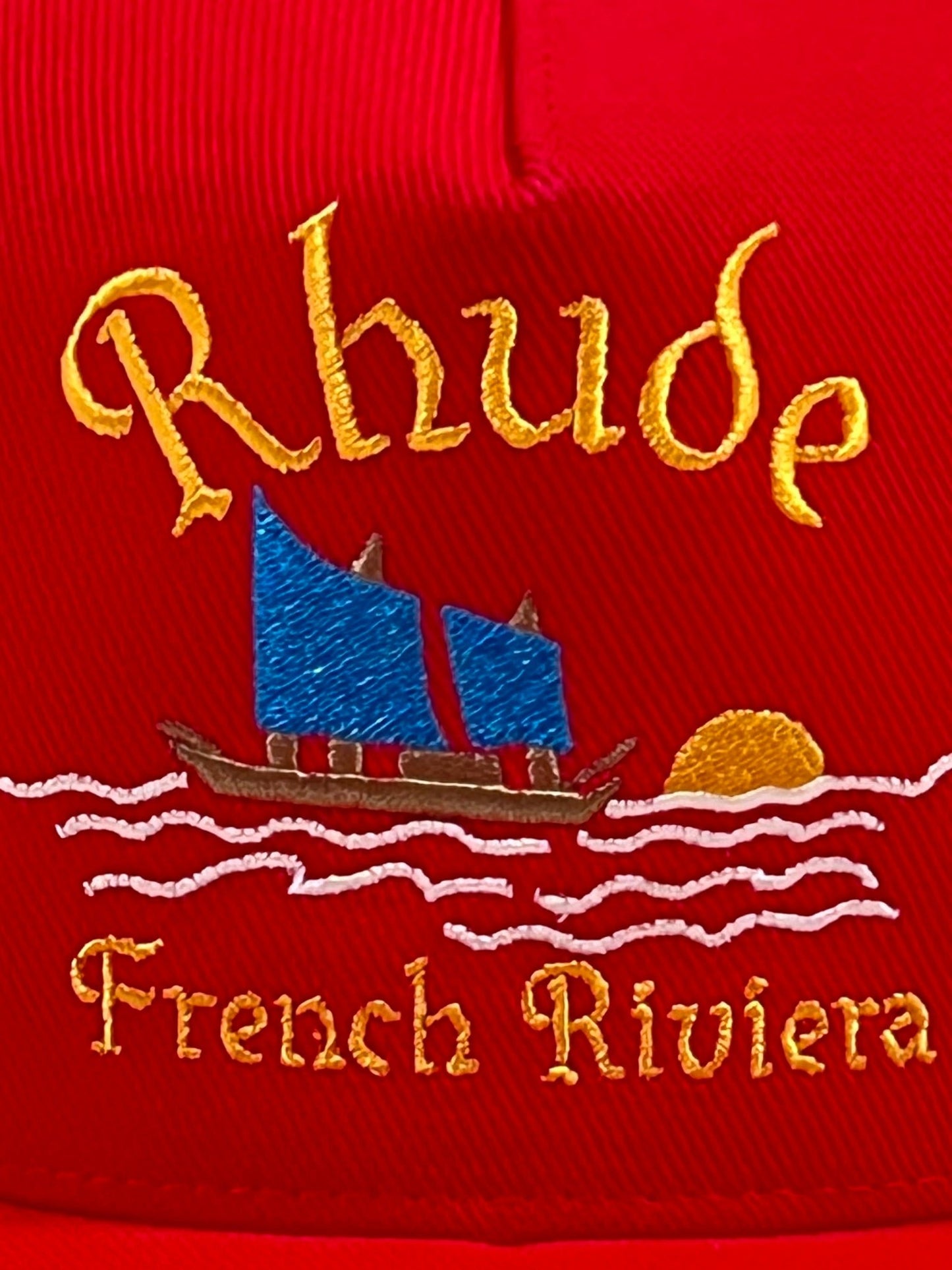 Embroidered RHUDE logo with the text "rhude french riviera" featuring a sailboat and sun design on a RHUDE RIVIERA SAILING HAT RED.