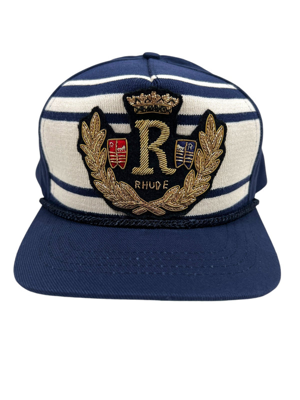 The RHUDE ROPE CREST STRUCTURE HAT NAVY by RHUDE showcases navy blue and white stripes with an embroidered "R" crest, complete with a crown and laurel wreath, as well as the word "RHUDE" below.