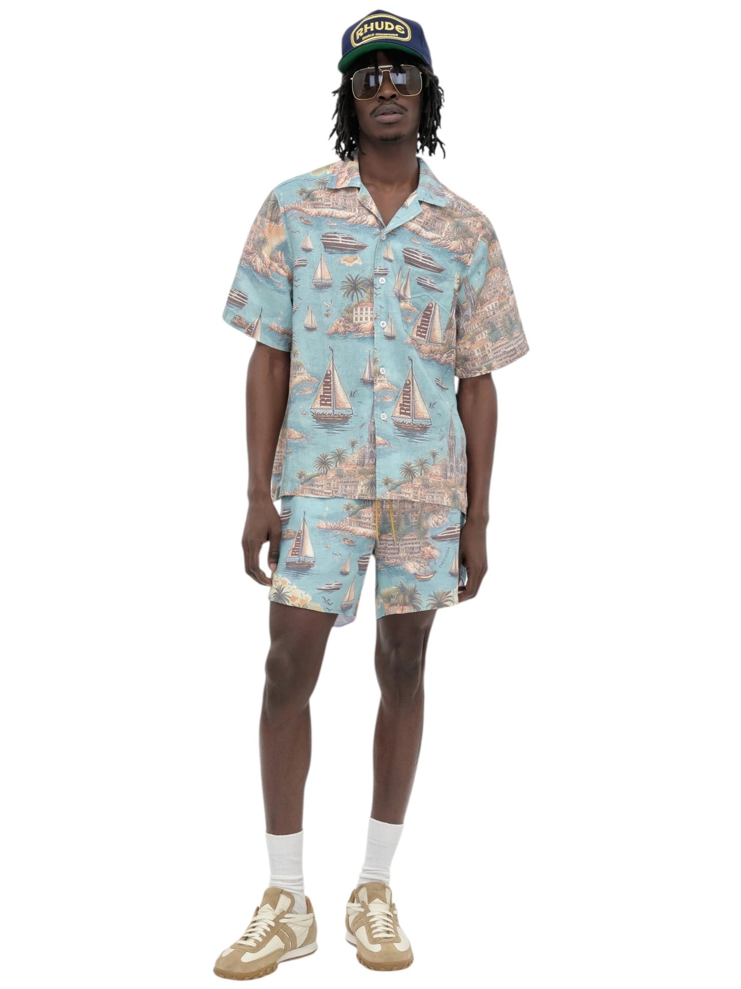 A person wears a RHUDE Rhude Sailing Map Shirt Multi and matching shorts, paired with sunglasses, a cap, white socks, and beige sneakers against a white background.