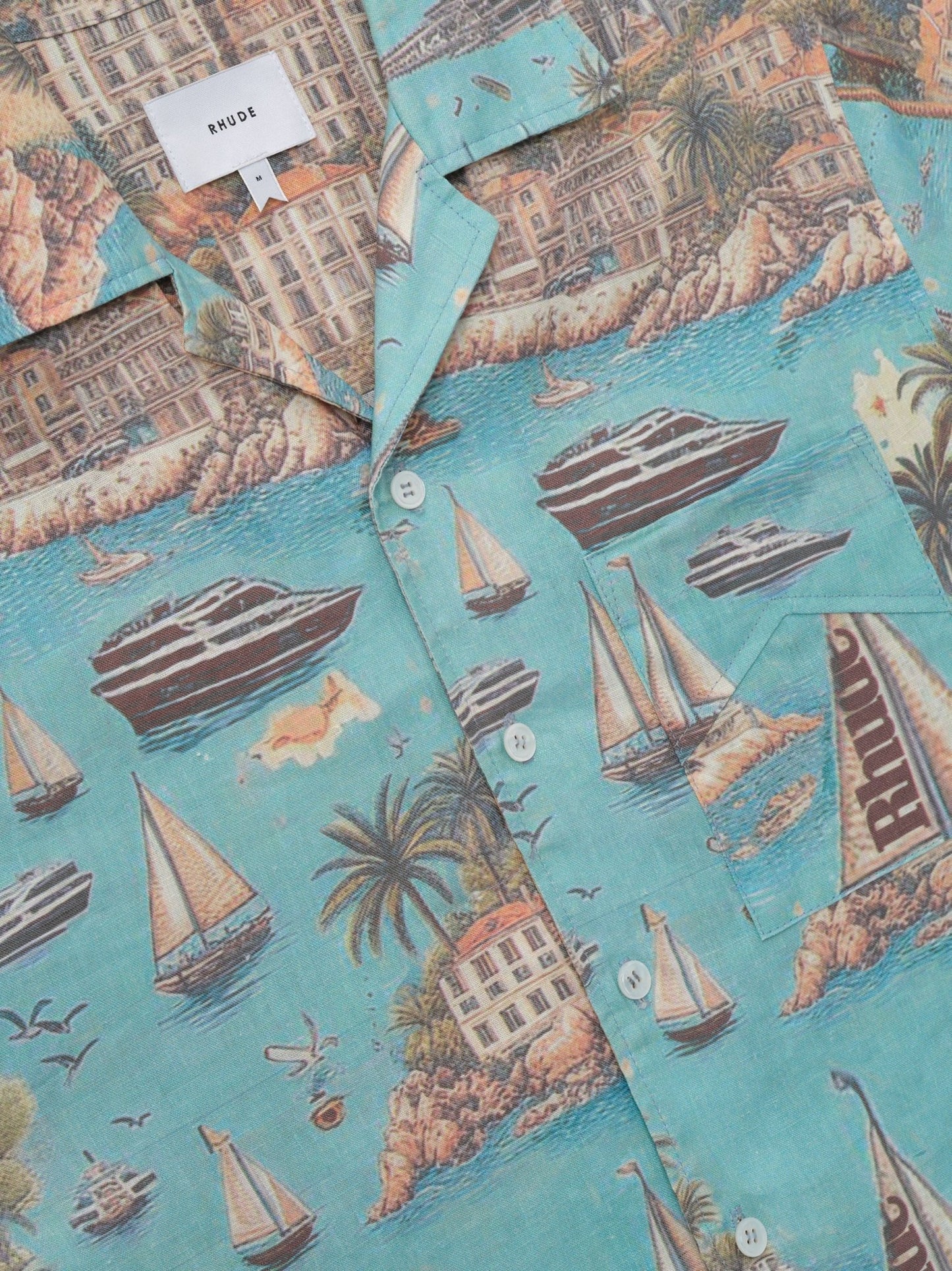 The Rhude Sailing Map Shirt Multi by RHUDE is a button-up featuring yachts, sailboats, birds, and tropical buildings on breathable linen with a serene blue background.