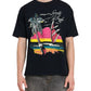 A person is wearing a black Rhude Saint-Rhude Tee by RHUDE, made from cotton jersey, featuring a colorful sunset graphic with palm trees and a sailboat, paired with gray cargo pants.