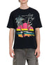 A person is wearing a black Rhude Saint-Rhude Tee by RHUDE, made from cotton jersey, featuring a colorful sunset graphic with palm trees and a sailboat, paired with gray cargo pants.