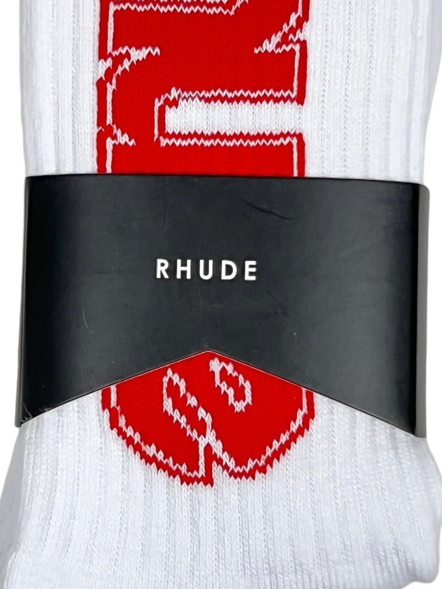 Close-up of a pair of RHUDE SKI CLUB SOCK WHITE by RHUDE, crafted from 60% cotton, featuring a large red design on a white background, wrapped in sleek black packaging.