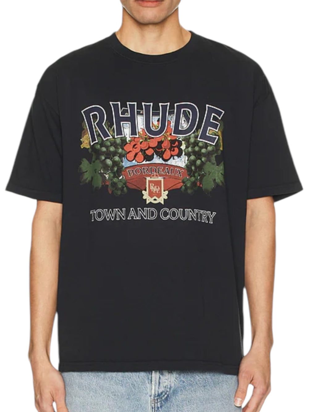 A person wearing the Rhude Town And Country Tee Vtg Blk, a high-quality cotton T-shirt from RHUDE, featuring a graphic logo with "RHUDE BORDEAUX TOWN AND COUNTRY" text and a floral design.