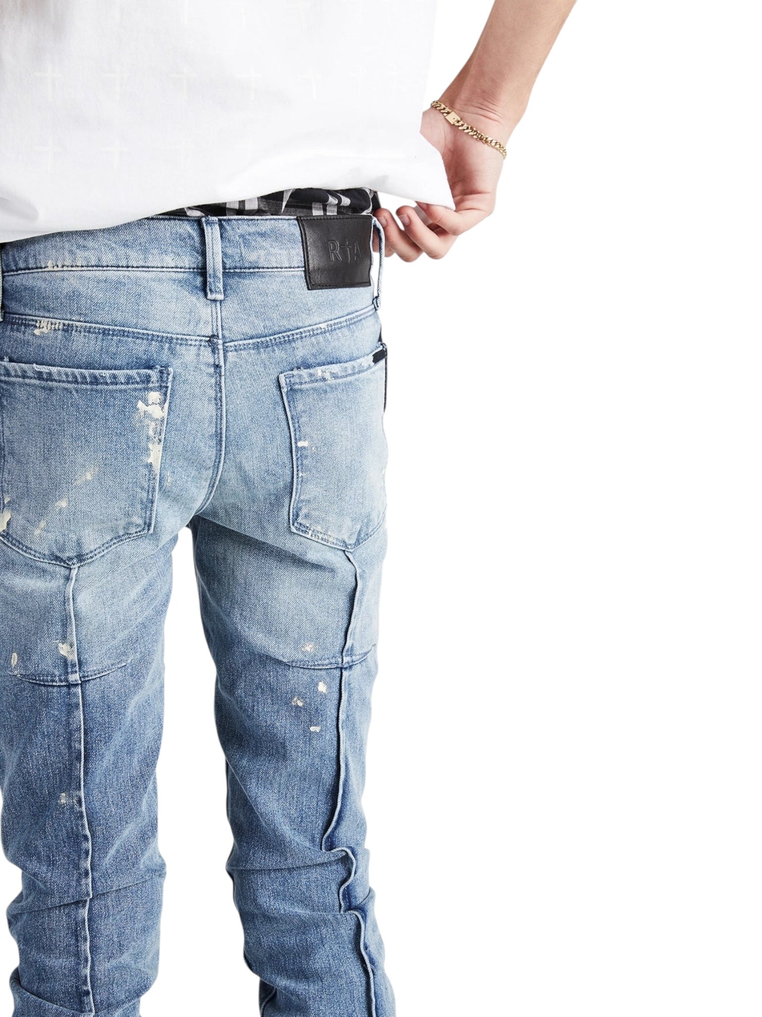 Model wears RTA Clayton Jean Distressed White Paint Blue by RTA—a light blue skinny jean with white paint details—paired with a white shirt for an easy, laid-back vibe, captured with their back turned and hand adjusting the waistband.