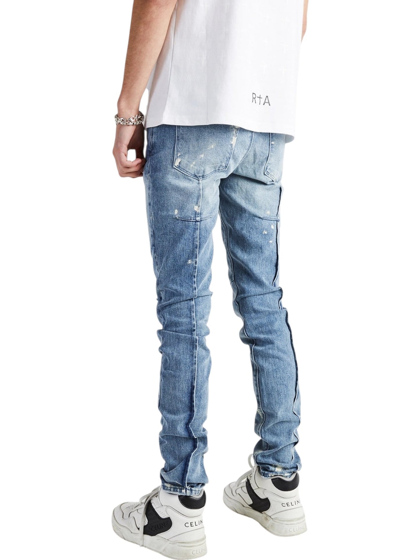 A person stands with their back to the camera, wearing a white t-shirt, RTA Clayton Jean Distressed White Paint Blue by RTA, and white sneakers.