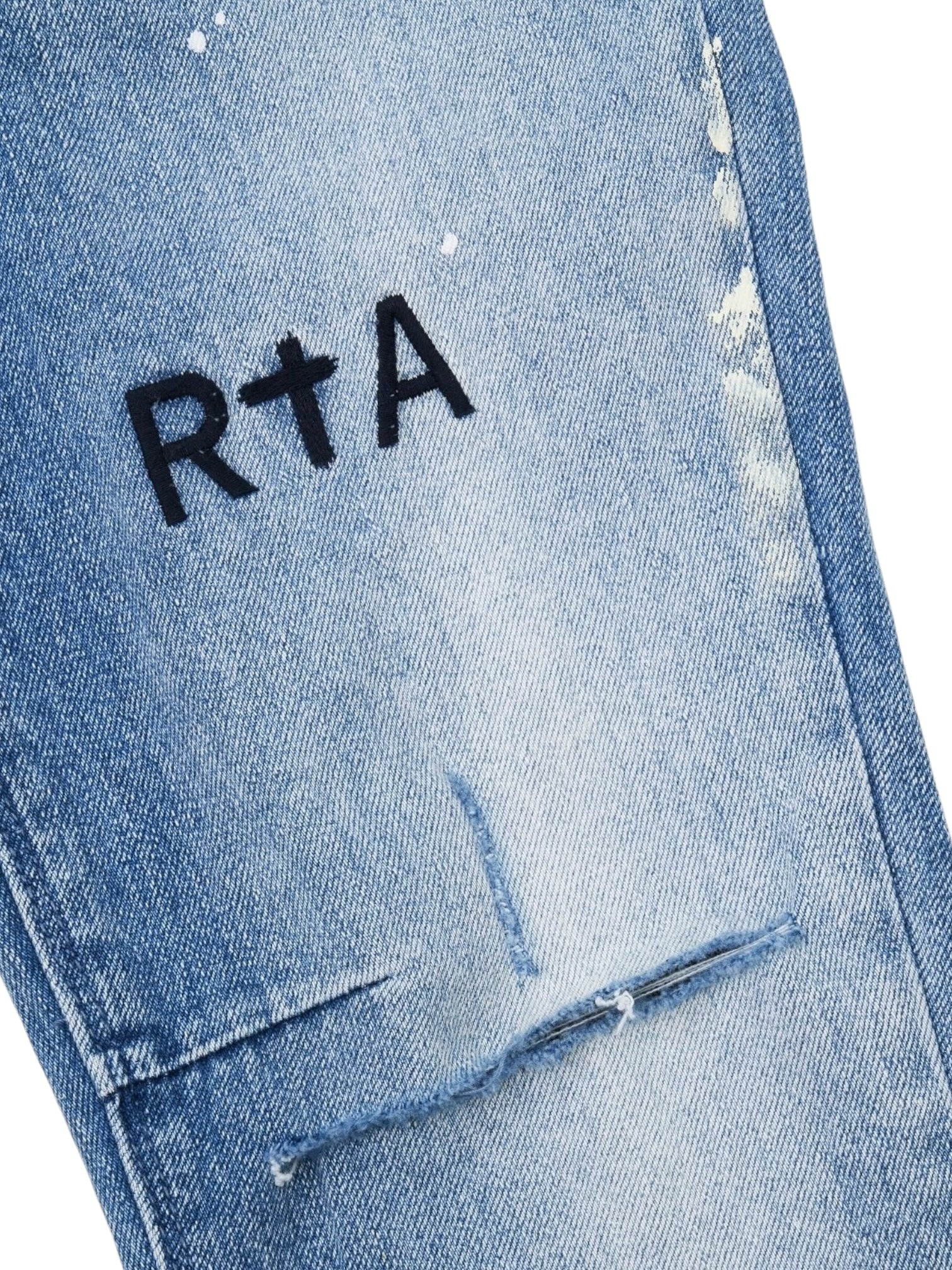 Close-up of RTA Clayton Jean Distressed White Paint Blue, featuring distressed white denim with blue paint accents and a black "R†A" logo embroidered above a ripped detail.