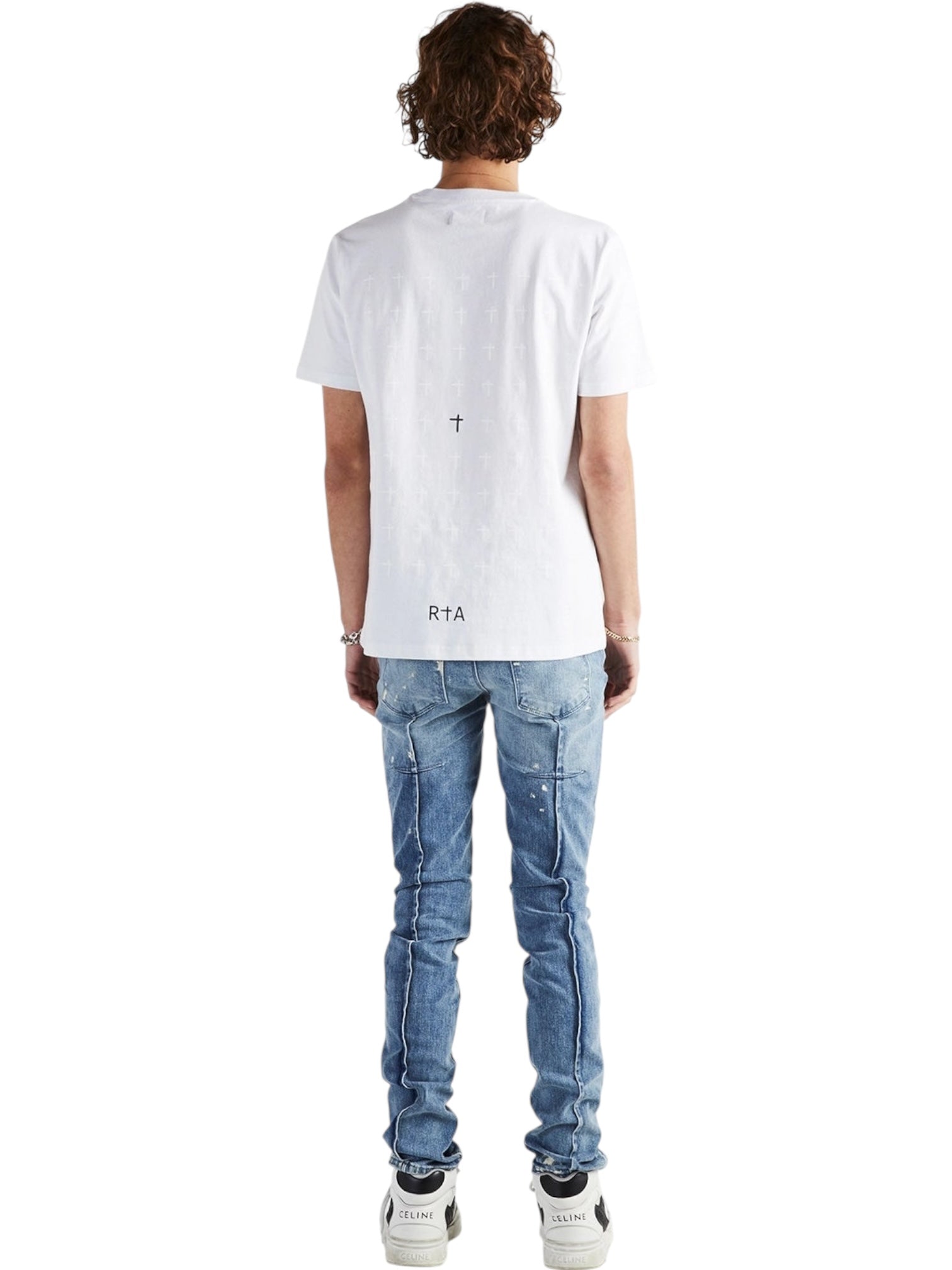 A person stands facing away, wearing a white T-shirt with small black text and a graphic on the back, RTA Clayton Jean Distressed White Paint Blue by RTA, and white sneakers, set against a plain white background.