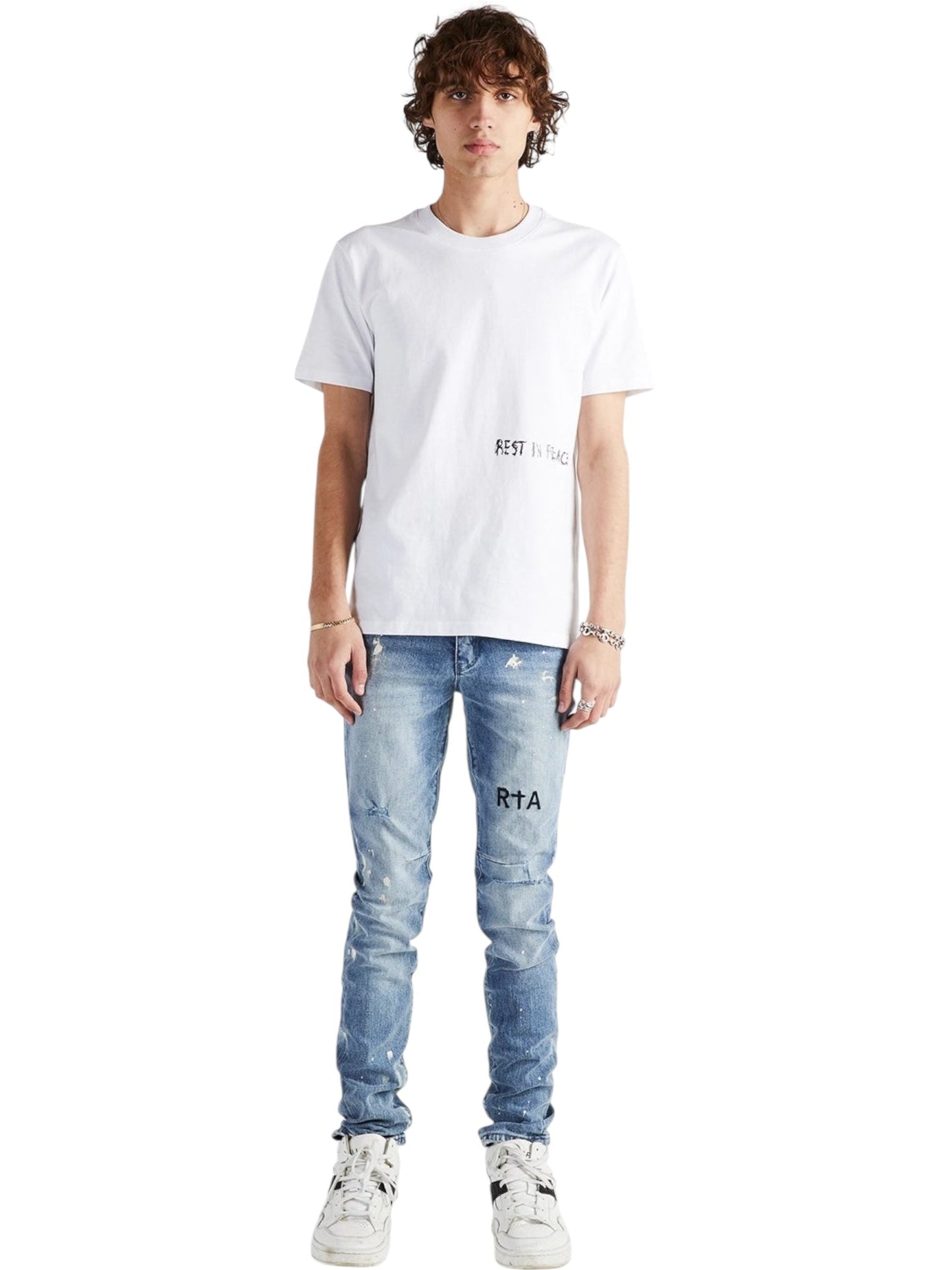 A person stands facing forward wearing a white "REST IN PEACE" T-shirt, RTA Clayton Jean Distressed White Paint Blue from RTA, and white sneakers against a plain white background.