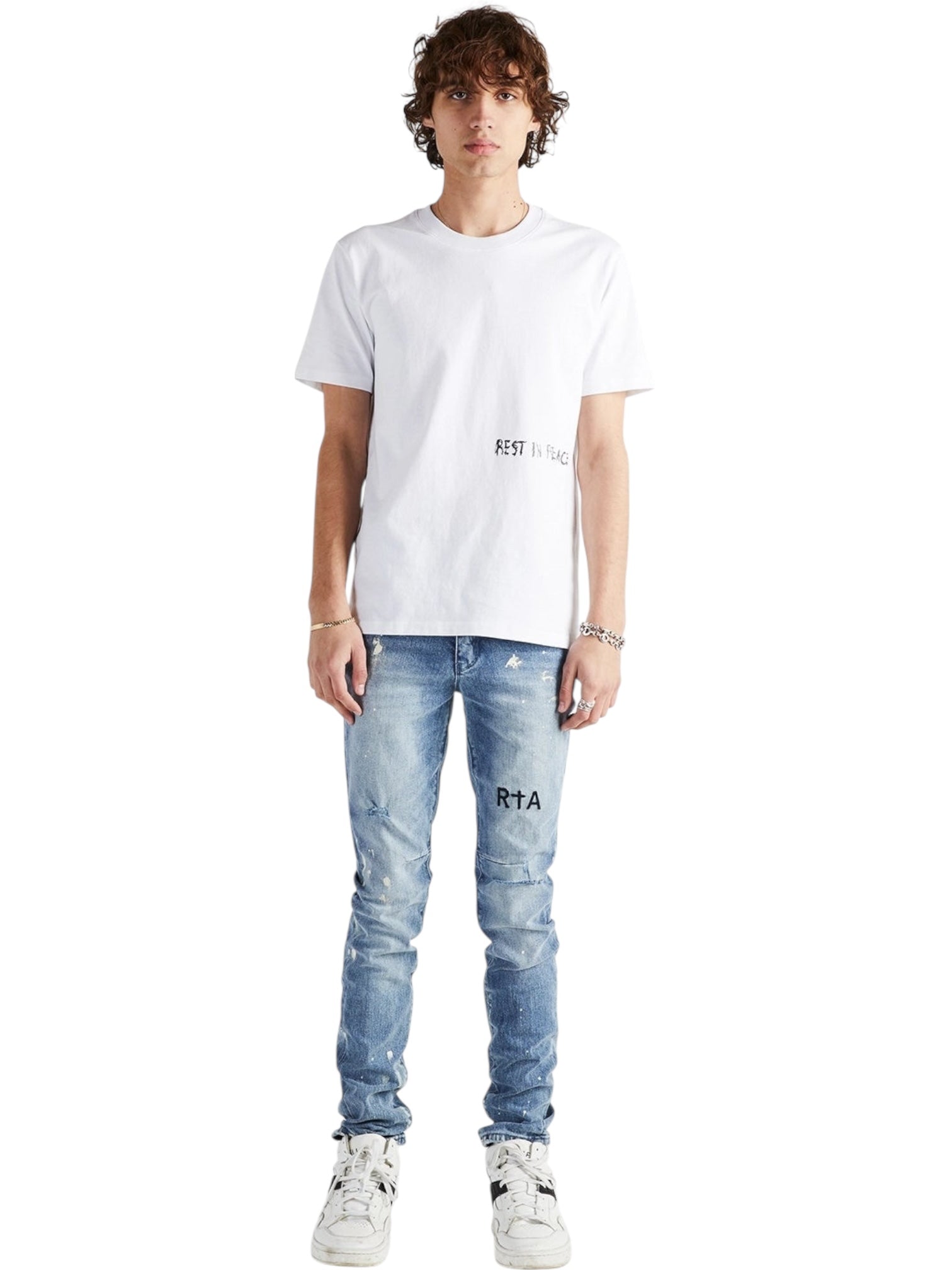 A person stands facing forward wearing a white "REST IN PEACE" T-shirt, RTA Clayton Jean Distressed White Paint Blue from RTA, and white sneakers against a plain white background.