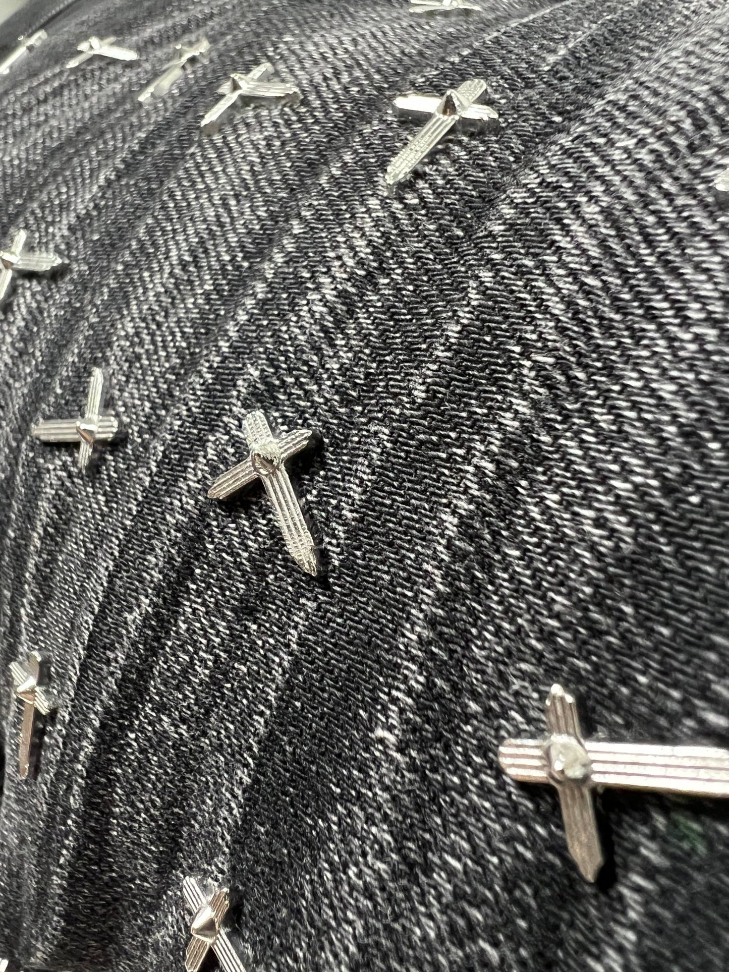 Close-up of RTA Olivier Stacked Graphite Fade Cross Black denim by RTA, showing black and white cotton fabric with multiple small metal cross-shaped studs.