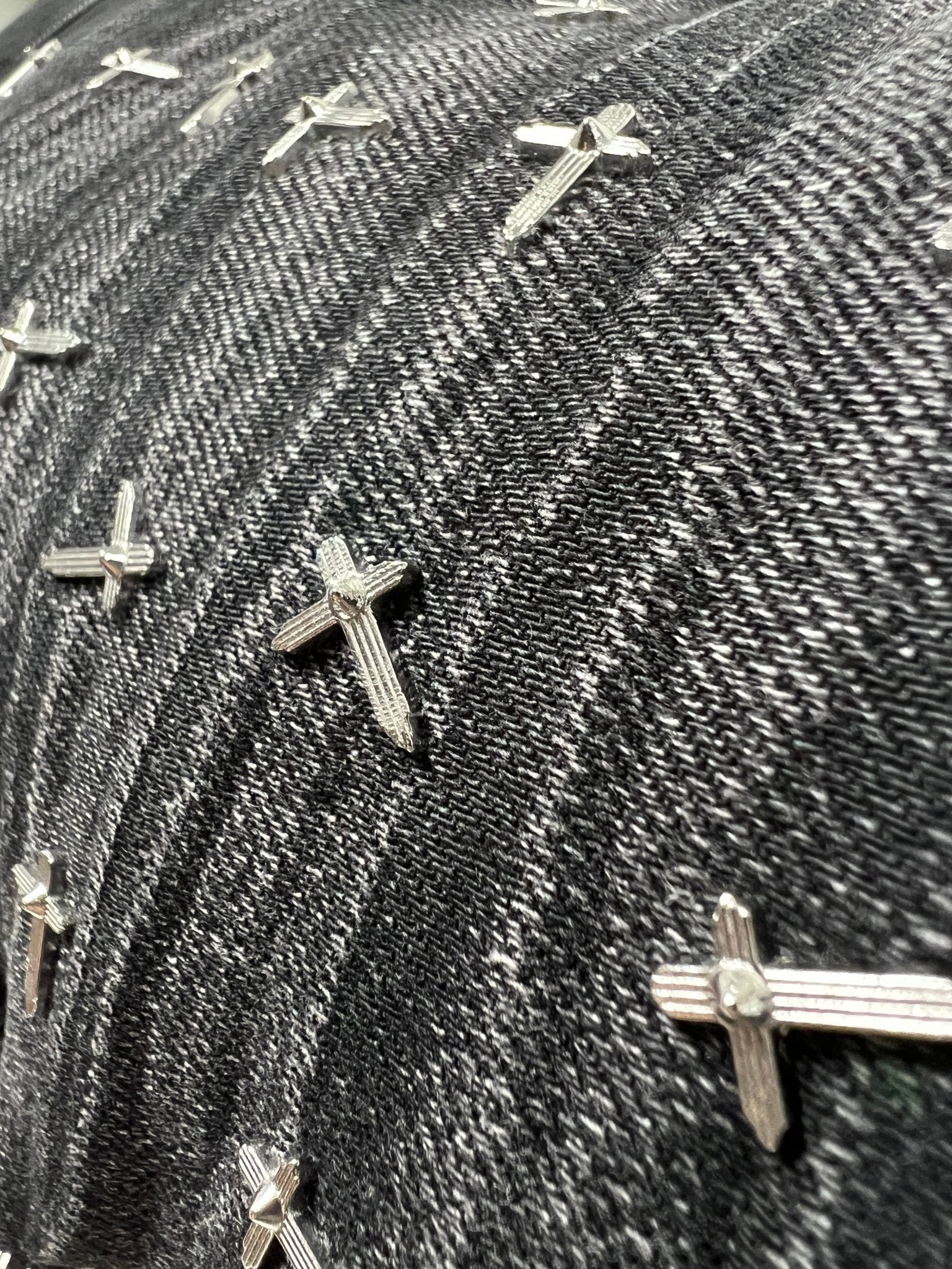 Close-up of RTA Olivier Stacked Graphite Fade Cross Black denim by RTA, showing black and white cotton fabric with multiple small metal cross-shaped studs.