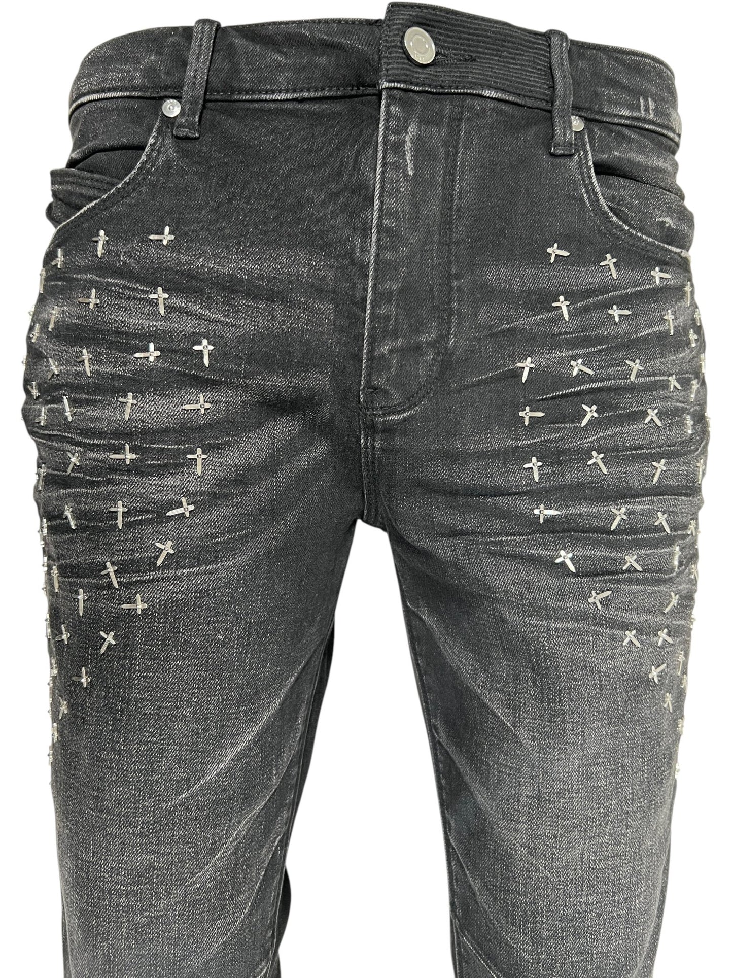 Close-up of RTA Olivier Stacked Graphite Fade Cross Black jeans by RTA, crafted from cotton denim with a graphite fade wash and silver cross-shaped studs in rows on the front upper thighs.