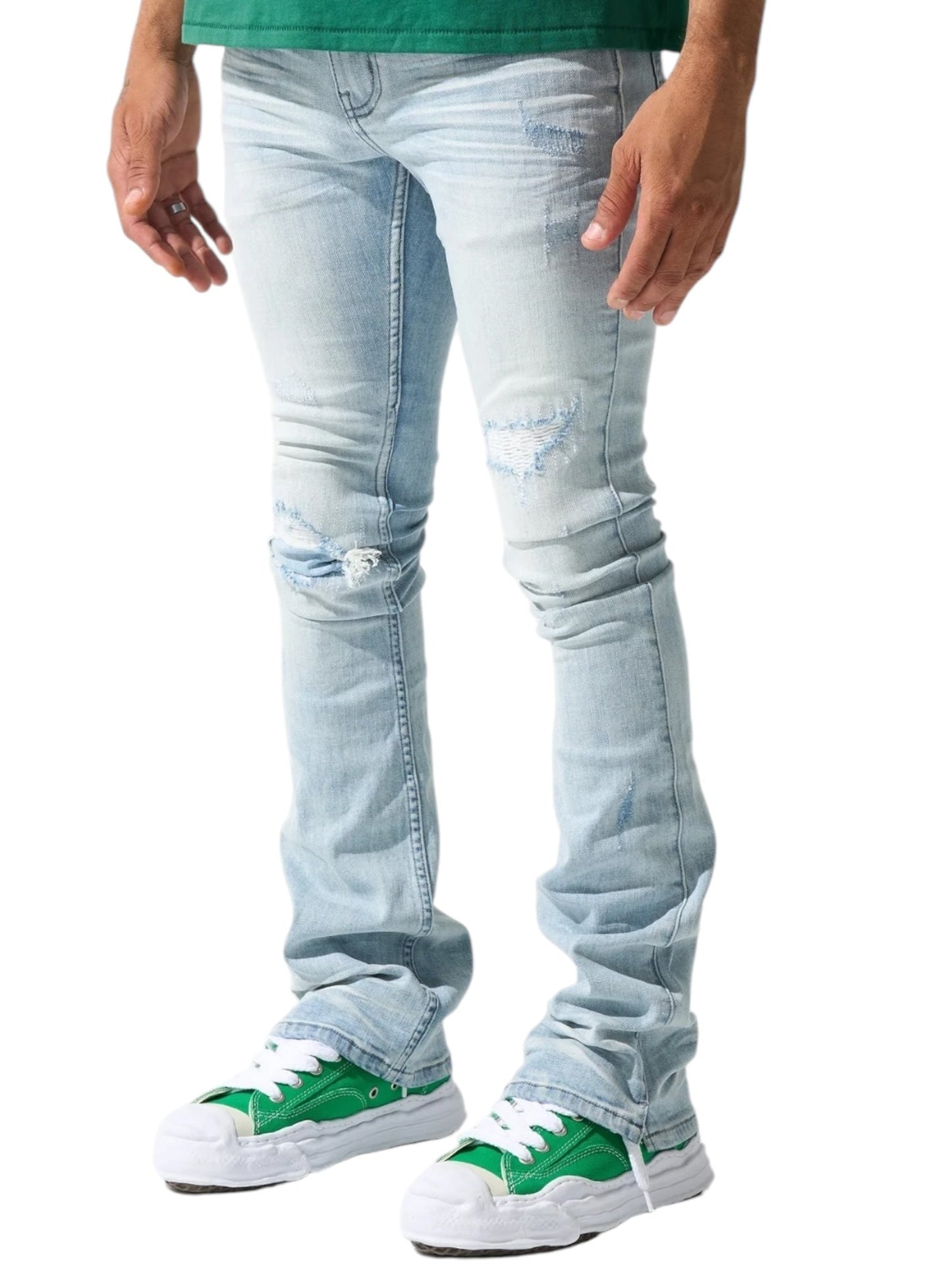 A man stands against a white background, wearing Serenede Azul Stacked Jeans Sky by SERENEDE, paired with a green shirt and green sneakers featuring white soles.