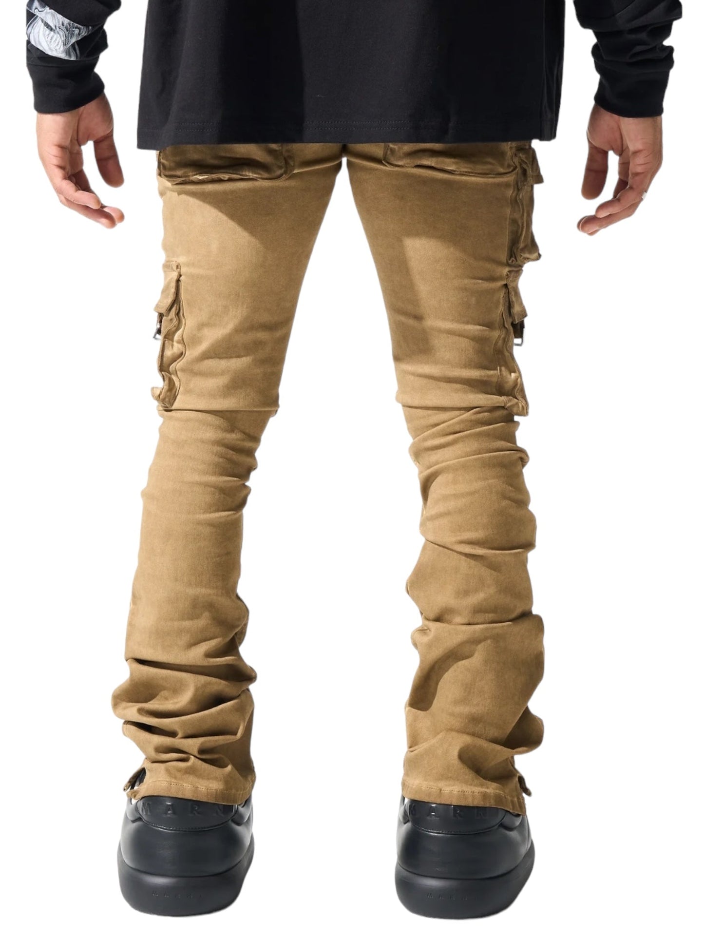 Back view of a person wearing SERENEDE CINNAMON CARGO STACKED BRWN pants from SERENEDE, featuring a leather logo patch, and black shoes.