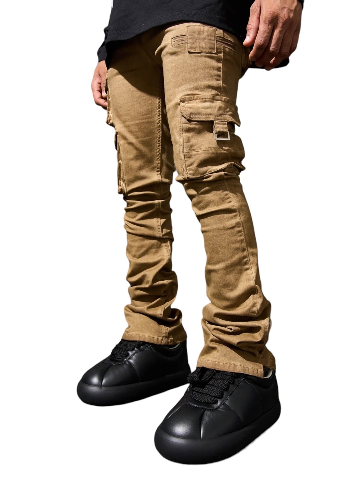 A person wearing SERENEDE CINNAMON CARGO STACKED BRWN pants with a leather logo patch and black sneakers is shown from the knees down.