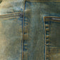 Close-up image of the back pocket and part of a side seam of SERENEDE KALAMATA JEANS OLIVE BROWN with visible stitching, showcasing a small button near the pocket and a subtle dirty washed effect by SERENEDE.