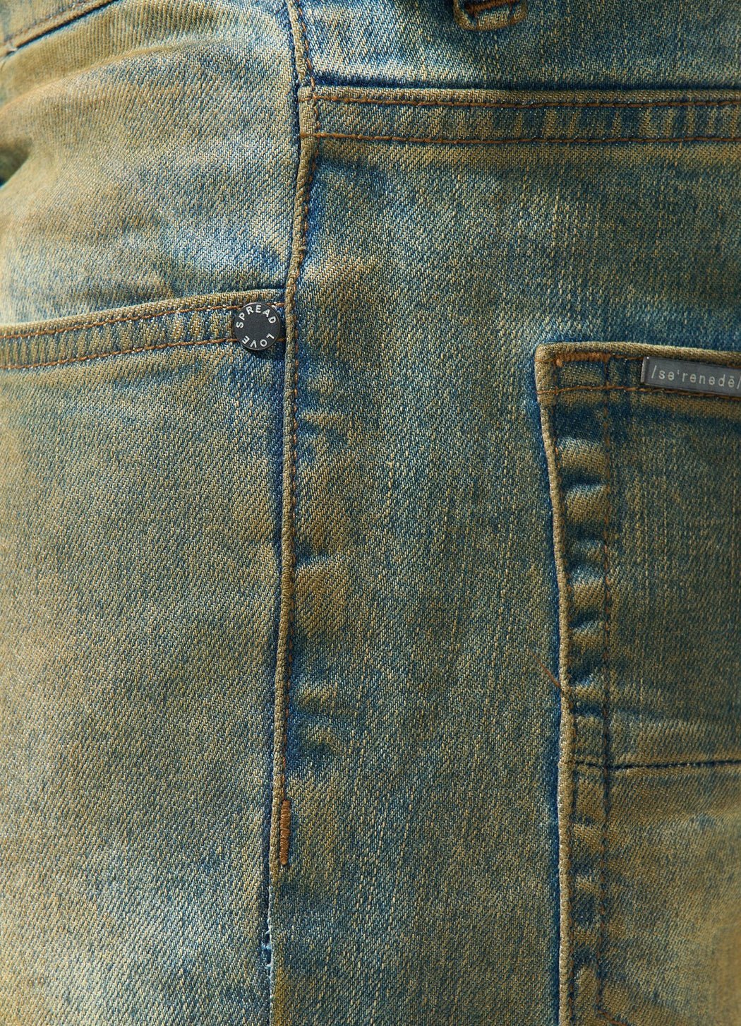 Close-up image of the back pocket and part of a side seam of SERENEDE KALAMATA JEANS OLIVE BROWN with visible stitching, showcasing a small button near the pocket and a subtle dirty washed effect by SERENEDE.