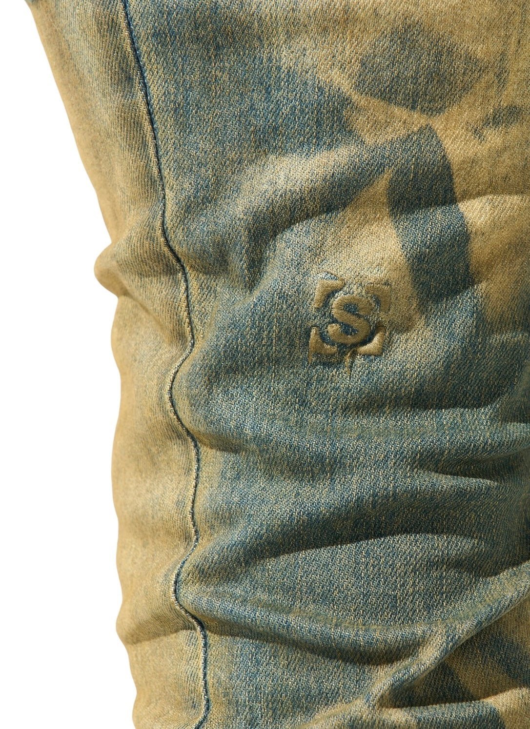 Close-up of faded blue denim fabric displaying a subtle embroidered logo, capturing the essence of SERENEDE KALAMATA JEANS OLIVE BROWN with a delicate dirty washed effect.