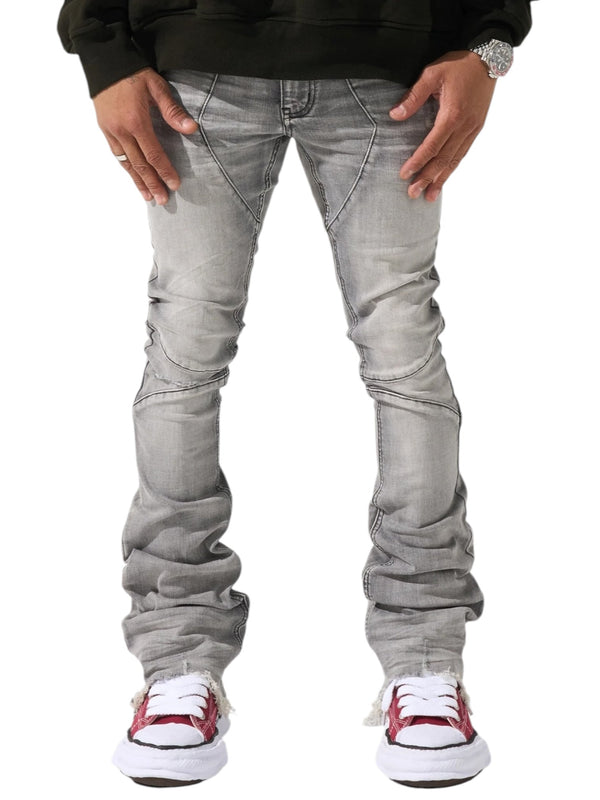 A person is seen from the waist down, wearing Serenede Noctis Stacked Jeans Grey by SERENEDE and red sneakers, set against a white background. The jeans are made of a comfortable cotton polyester spandex blend with a faded gray finish.