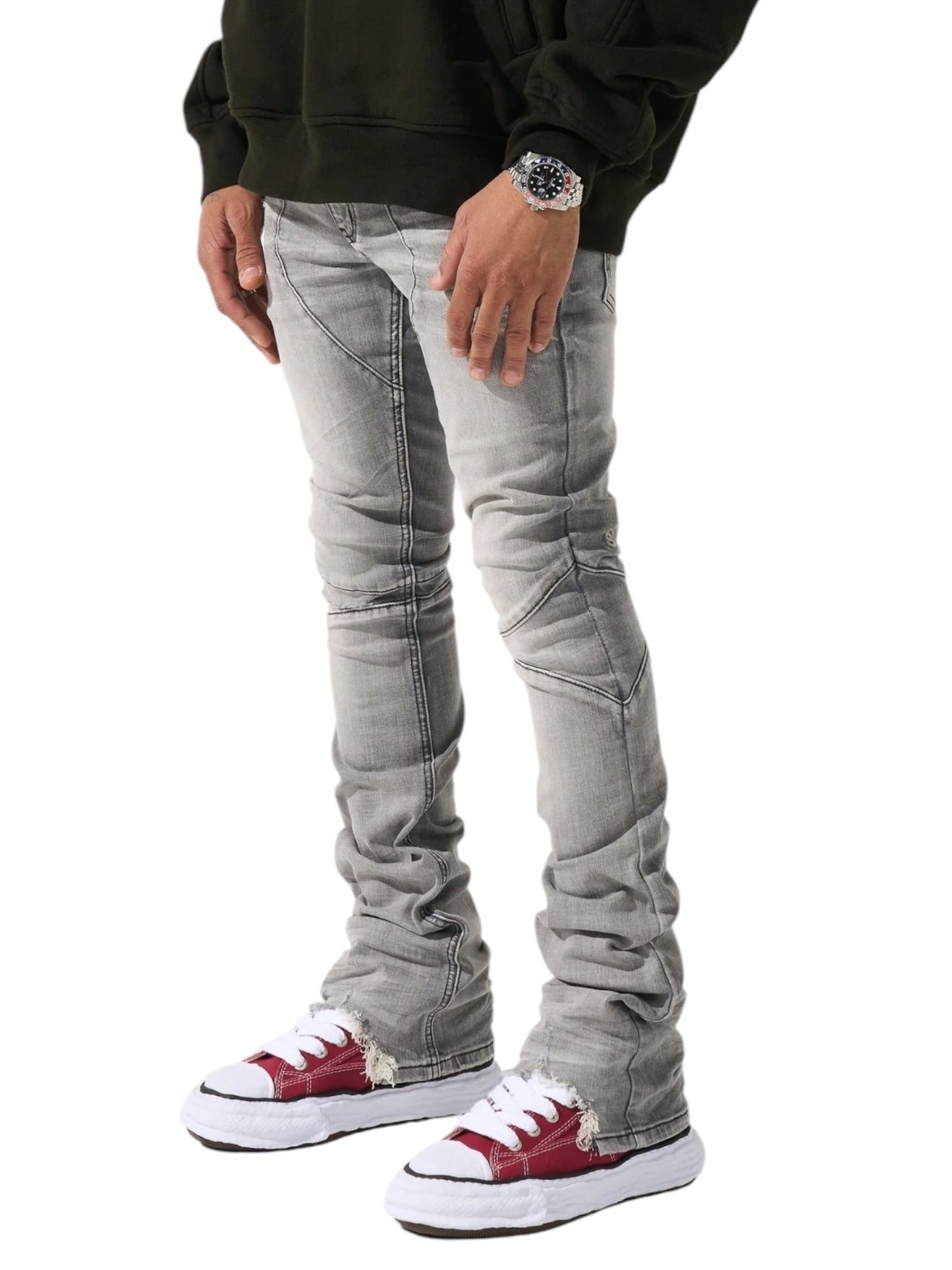 A person stands against a white background wearing a dark sweater, SERENEDE Noctis Stacked Jeans Grey with light gray stitching, red and white sneakers, and a wristwatch.