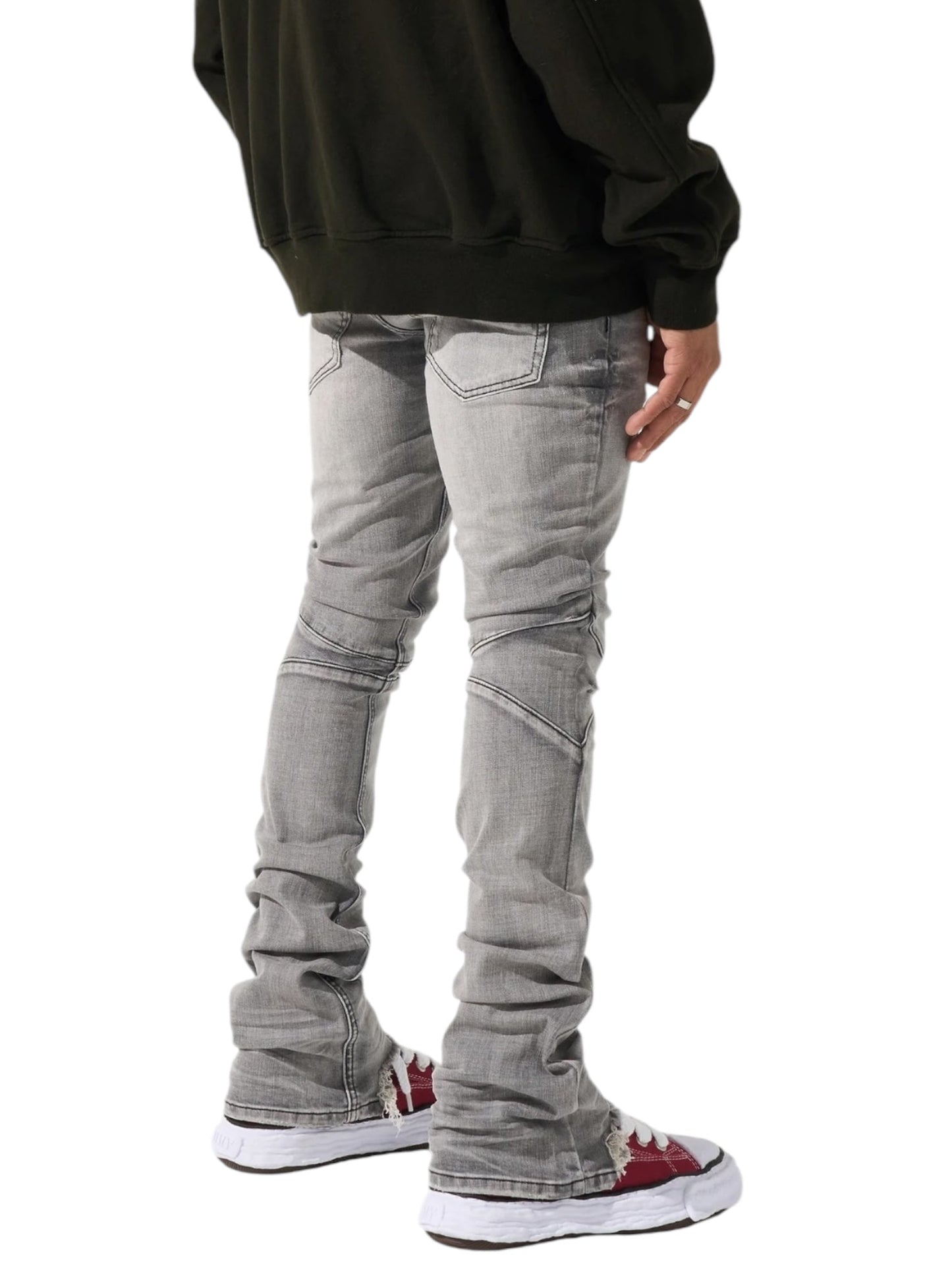 A person, seen from the side, is dressed in a dark hoodie, SERENEDE Noctis Stacked Jeans Grey, and white sneakers featuring red accents.