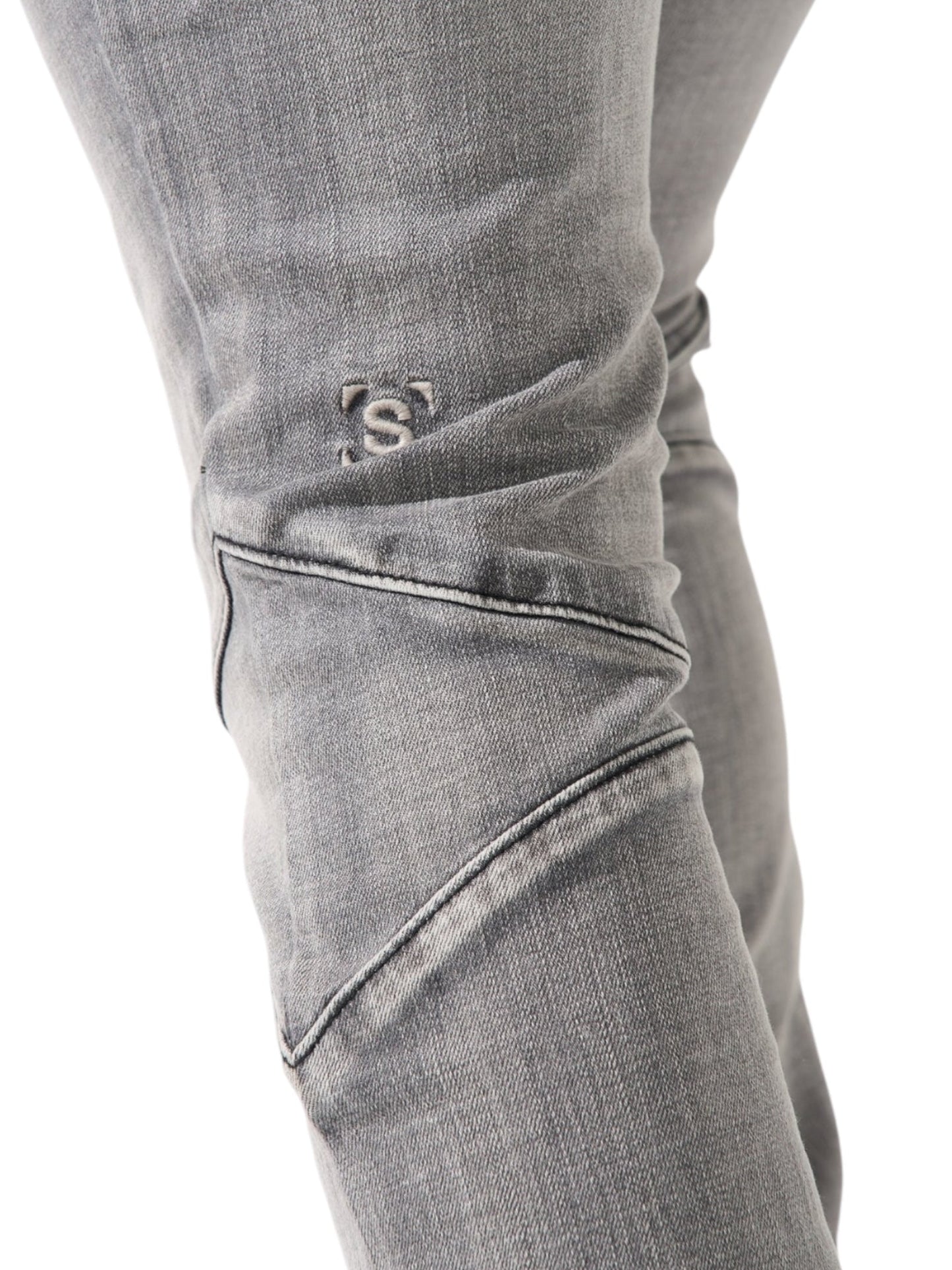 Close-up of a person's leg in SERENEDE Noctis Stacked Jeans Grey, featuring detailed stitching and a subtle embroidered 'S'.