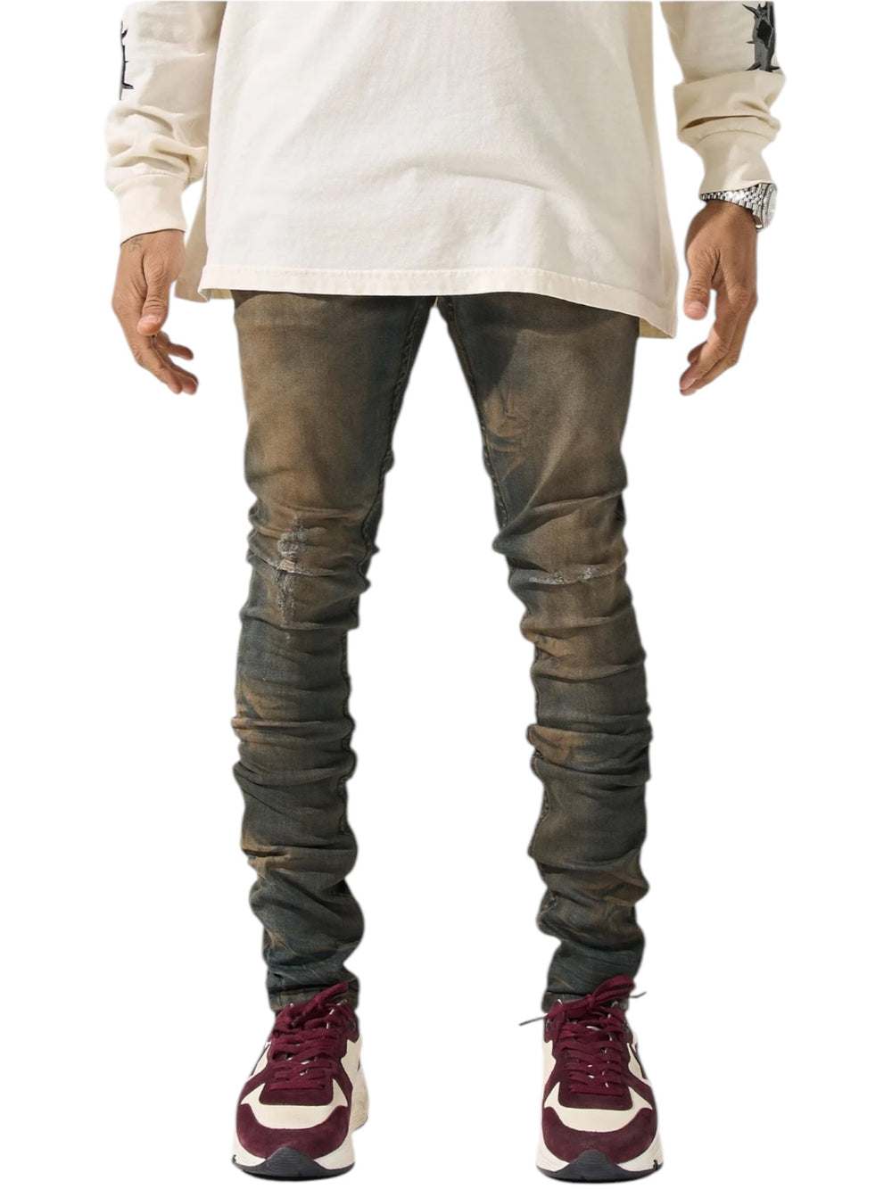 A person stands with hands at their sides, wearing a long-sleeved beige shirt paired with SERENEDE's Serenede Oud Jeans Oudwood, dark-washed distressed brown skinny fit jeans. Their ensemble is completed by maroon and beige sneakers.