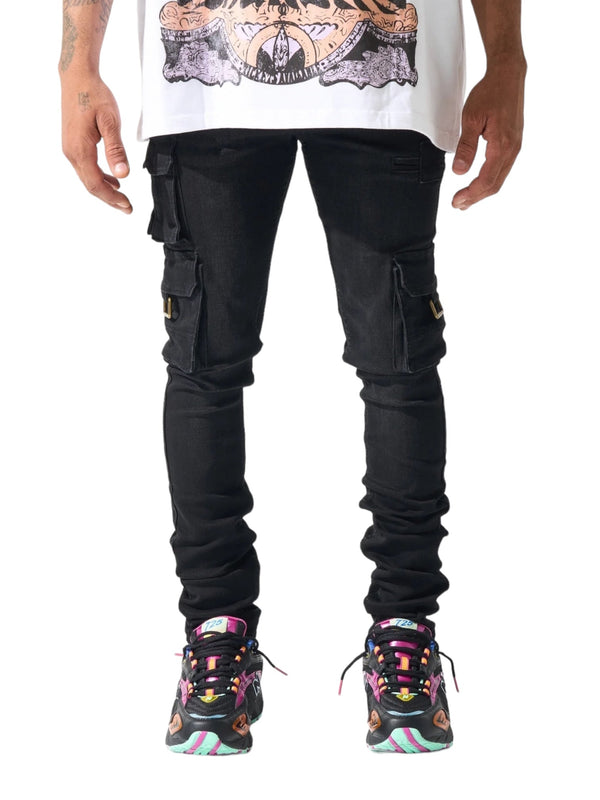 A person wearing a graphic t-shirt, SERENEDE Panthera Cargo Jeans in Washed Black, and multicolored sneakers stands facing the camera. Only the torso and legs are visible against a white background.